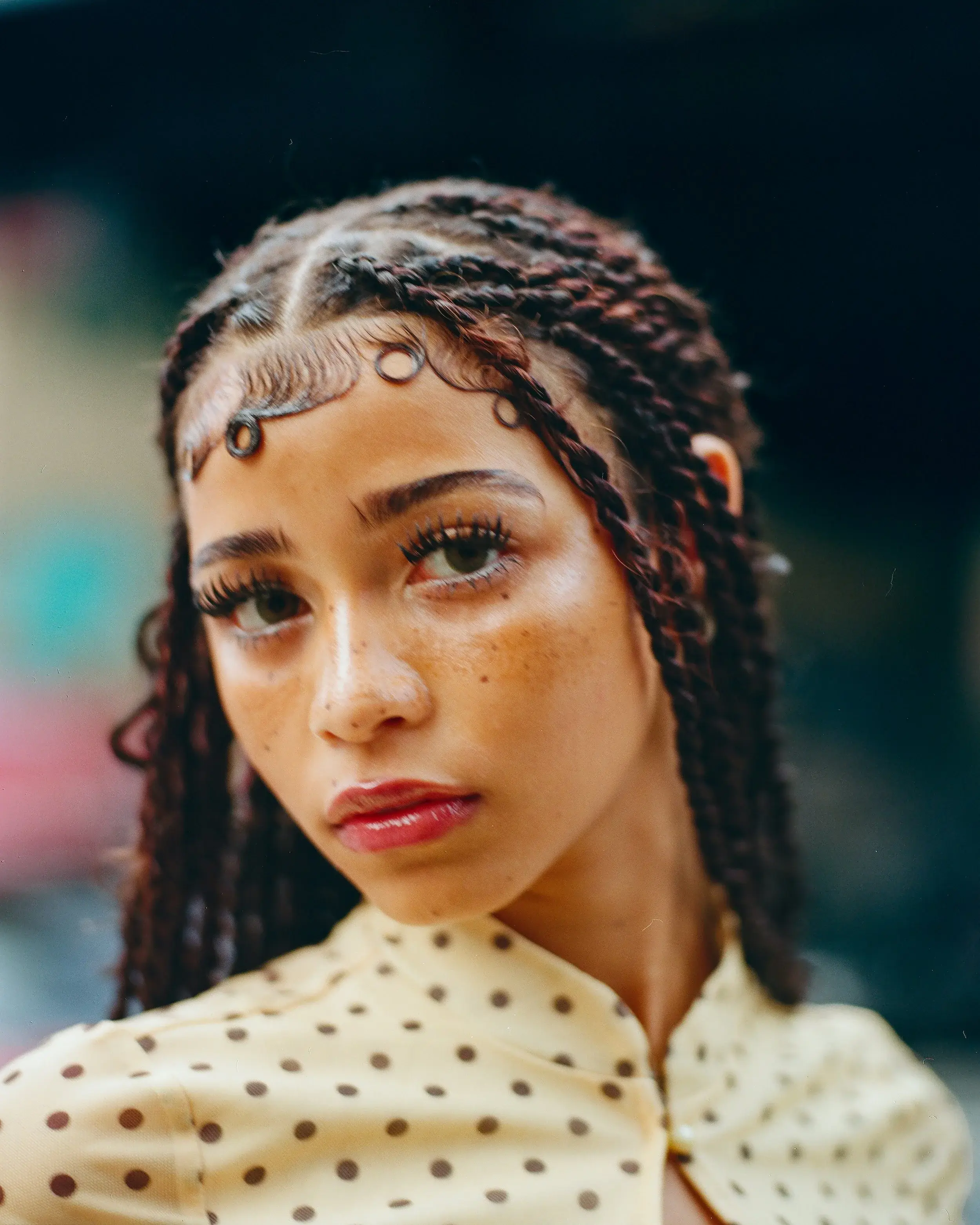 Close portrait of a young woman with braids and freckles in a polka-dot blouse