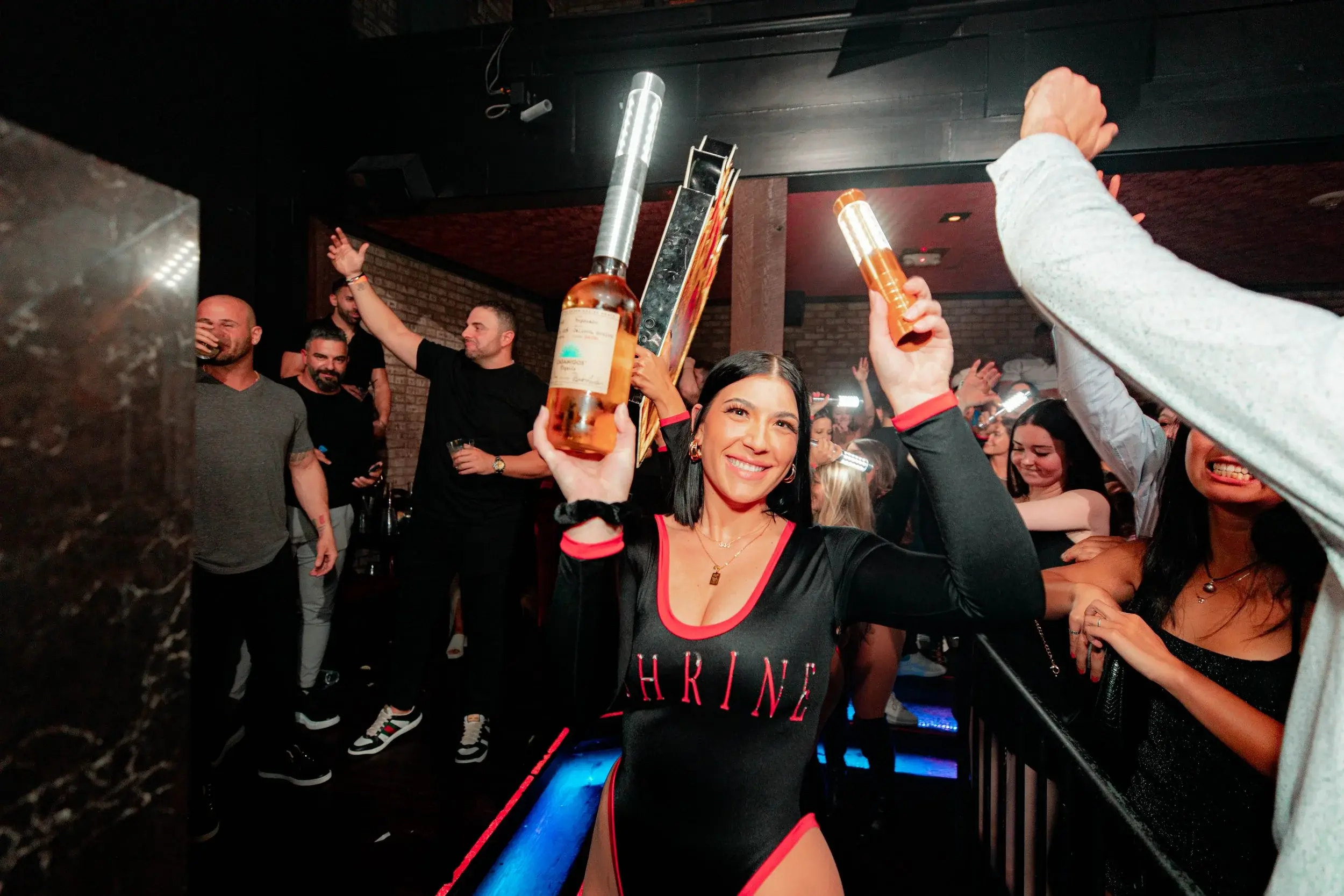 Bottle service staff raising sparkler-topped bottles above a cheering nightclub crowd