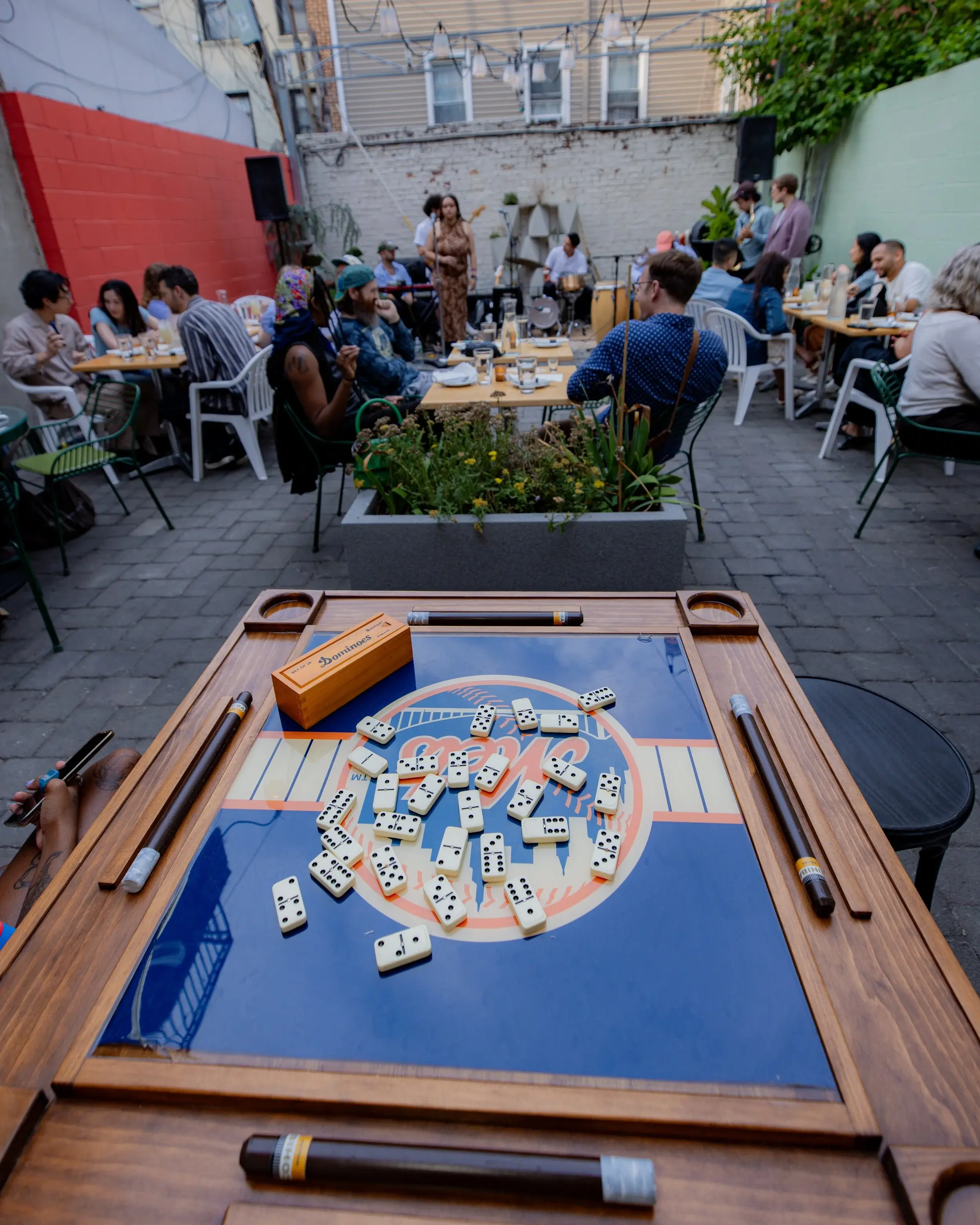 Domino table in the foreground of a lively courtyard gathering with seated guests