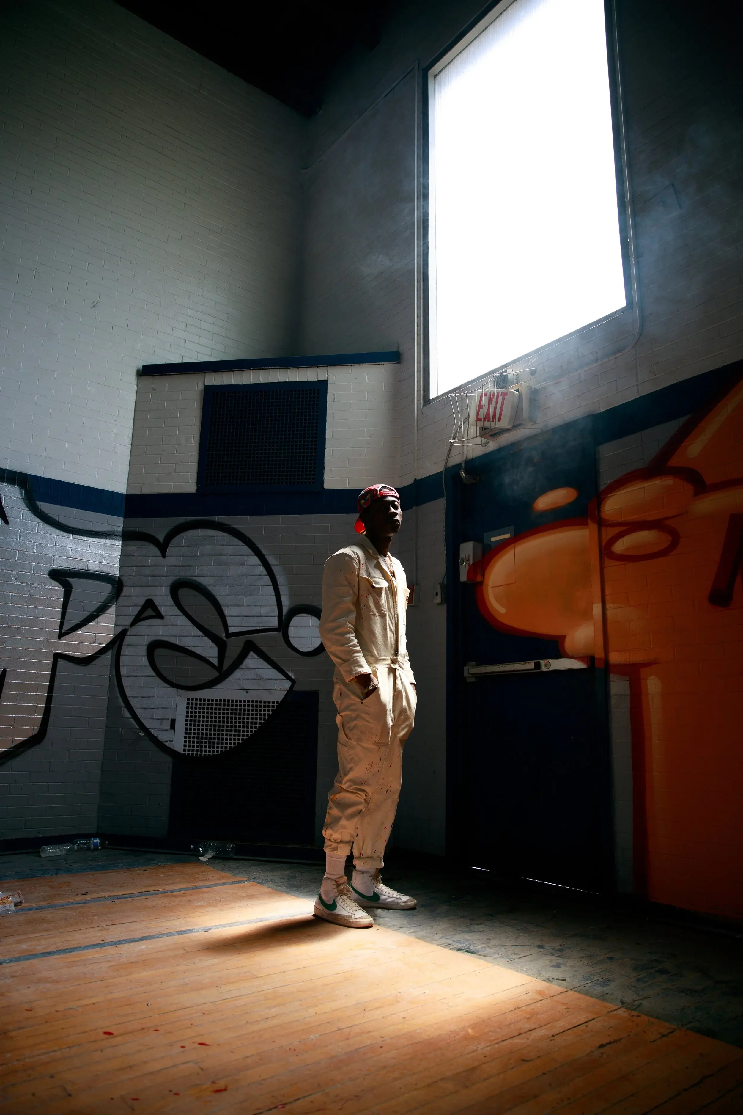 Lookbook shot of a model standing beneath a bright window in a graffiti-lined gym