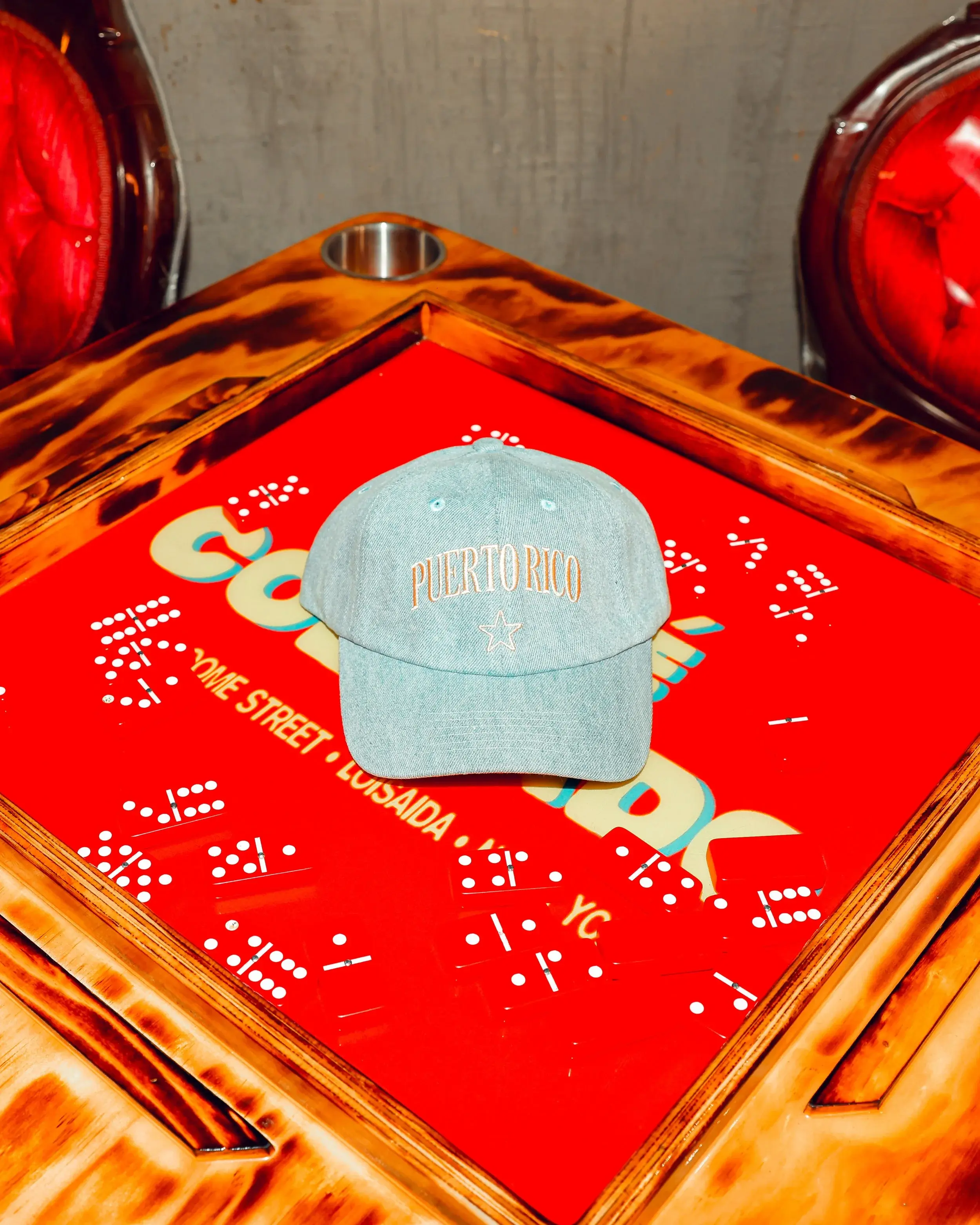 Embroidered denim cap displayed on a glossy red domino tabletop between tufted chairs
