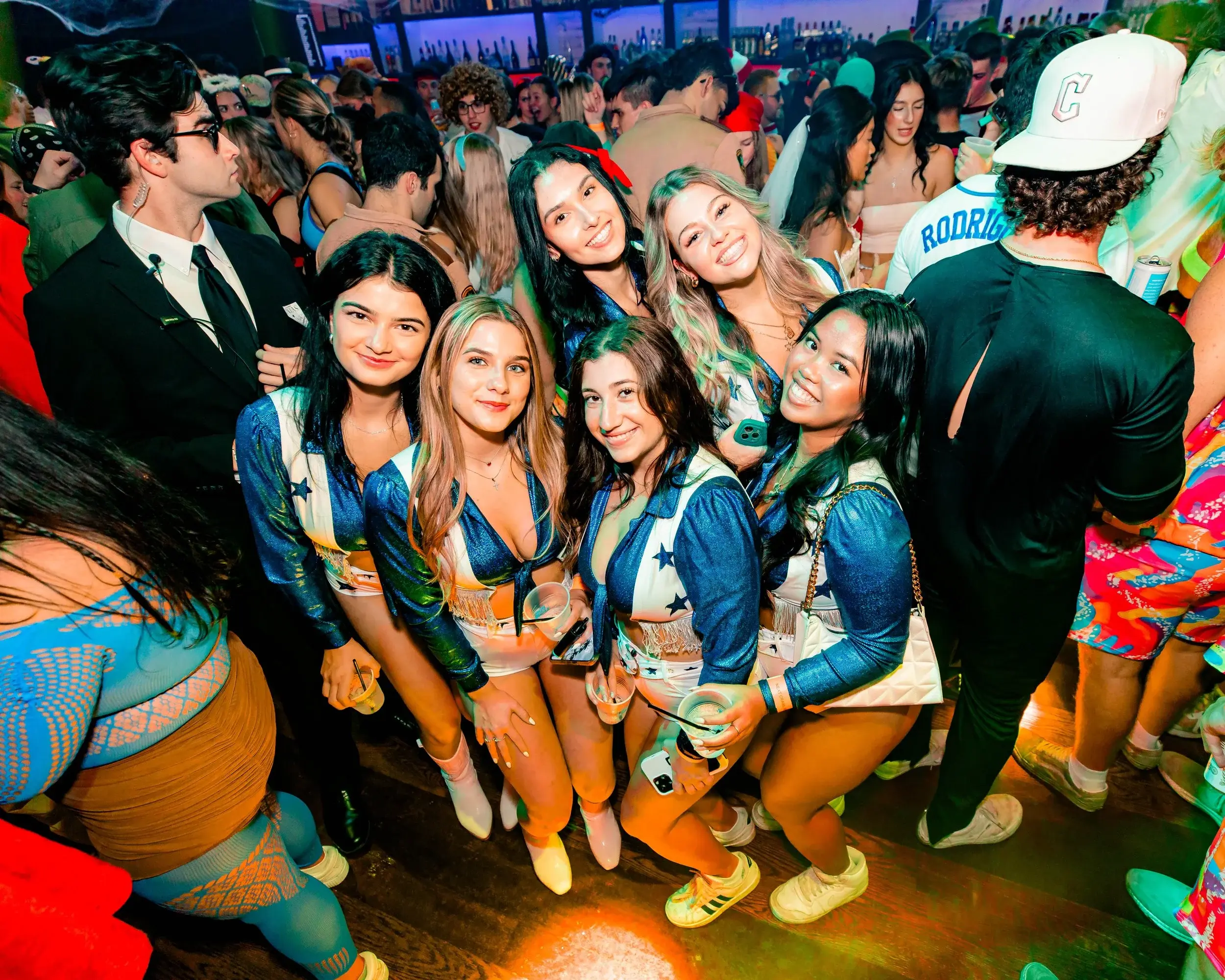 Group of friends in matching cheerleader costumes posing together on a packed club floor