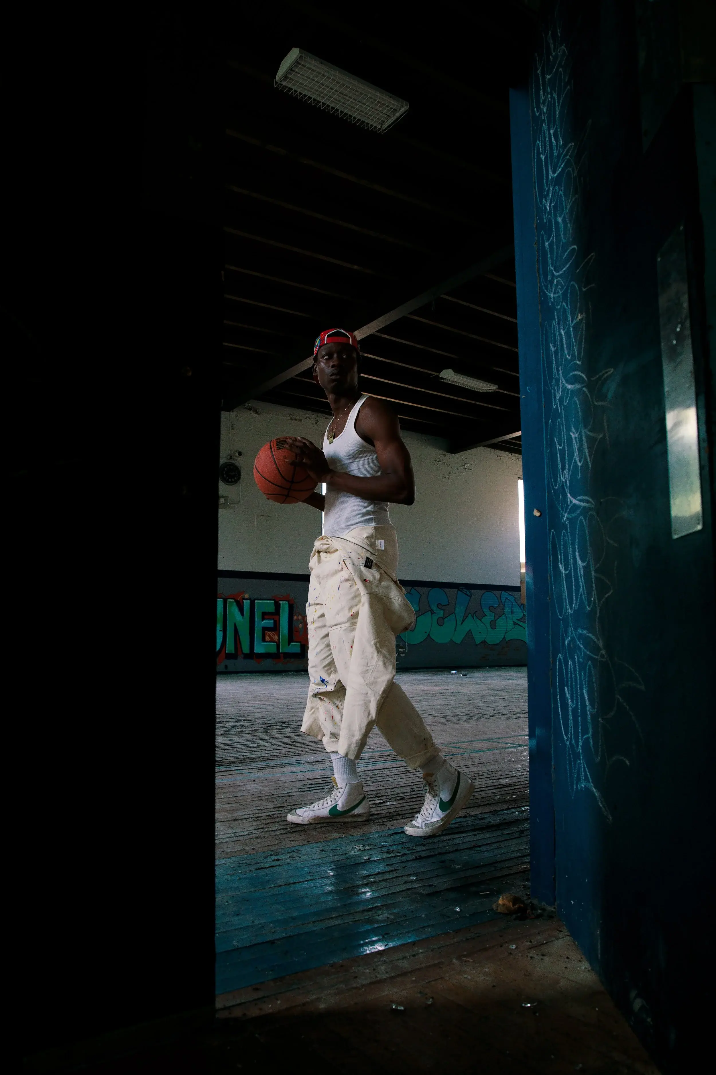 Model in a white tank top and cargo pants holding a basketball, framed by a doorway