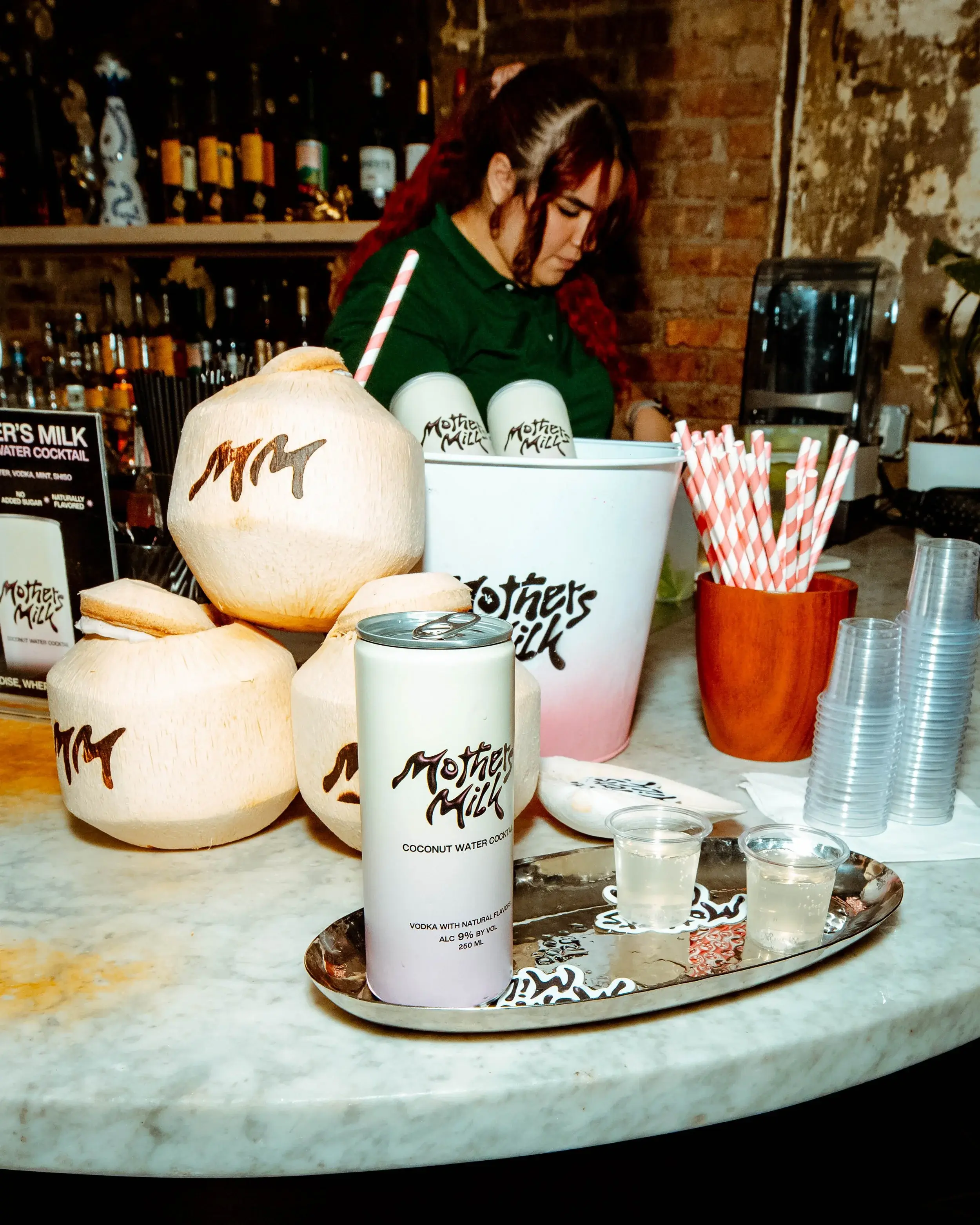 Bartender preparing coconut drinks beside canned cocktails and striped straws at a party