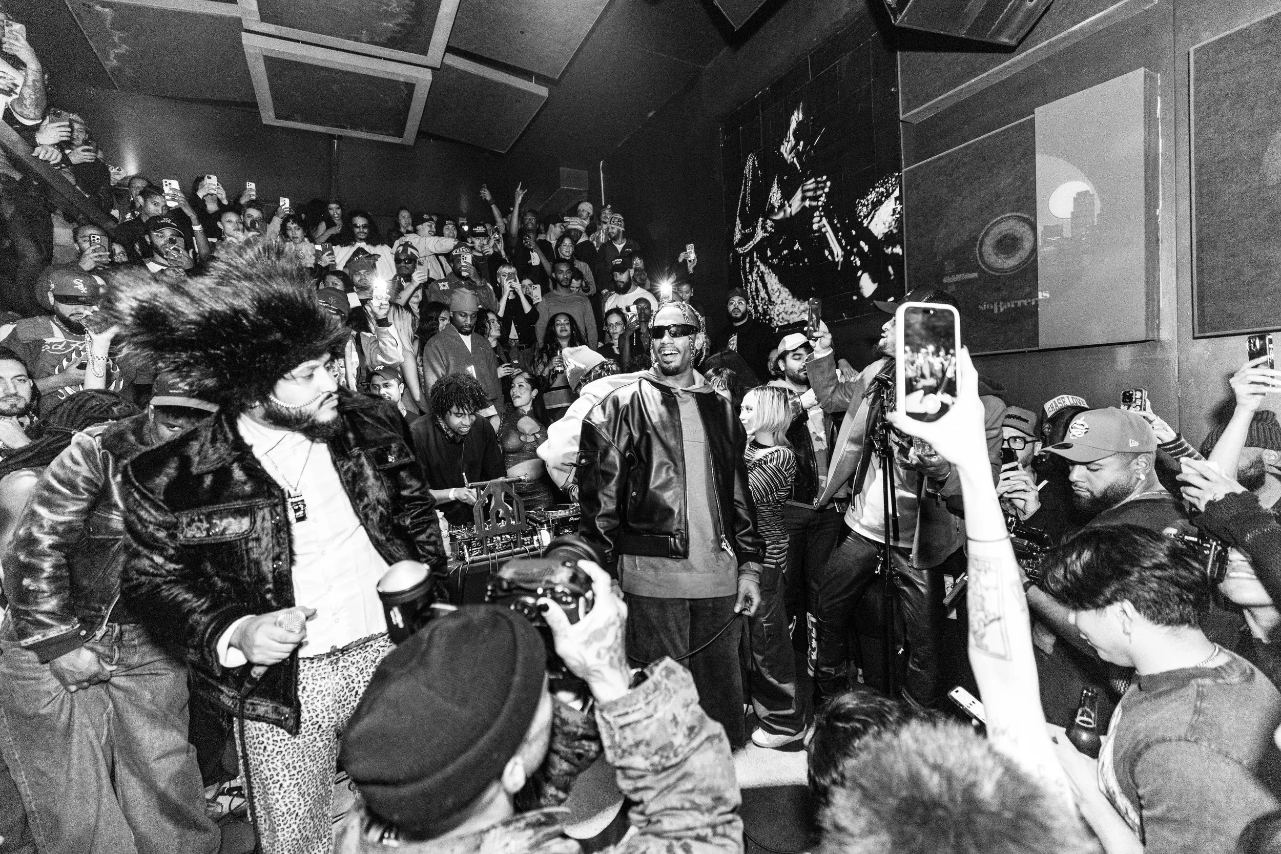 Black and white scene of a performer holding a microphone surrounded by clubgoers