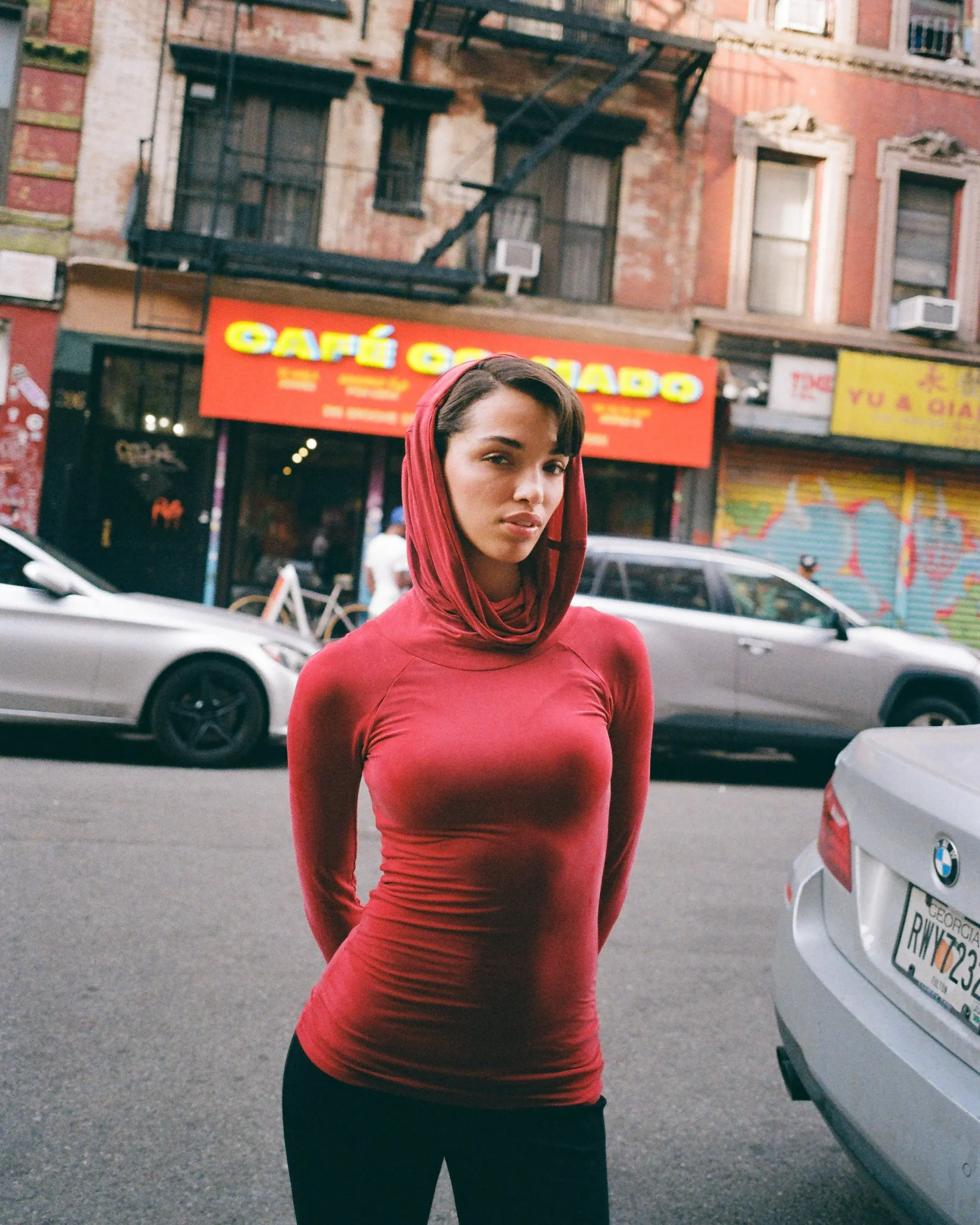 Street portrait of a woman in a fitted red hood standing between parked cars