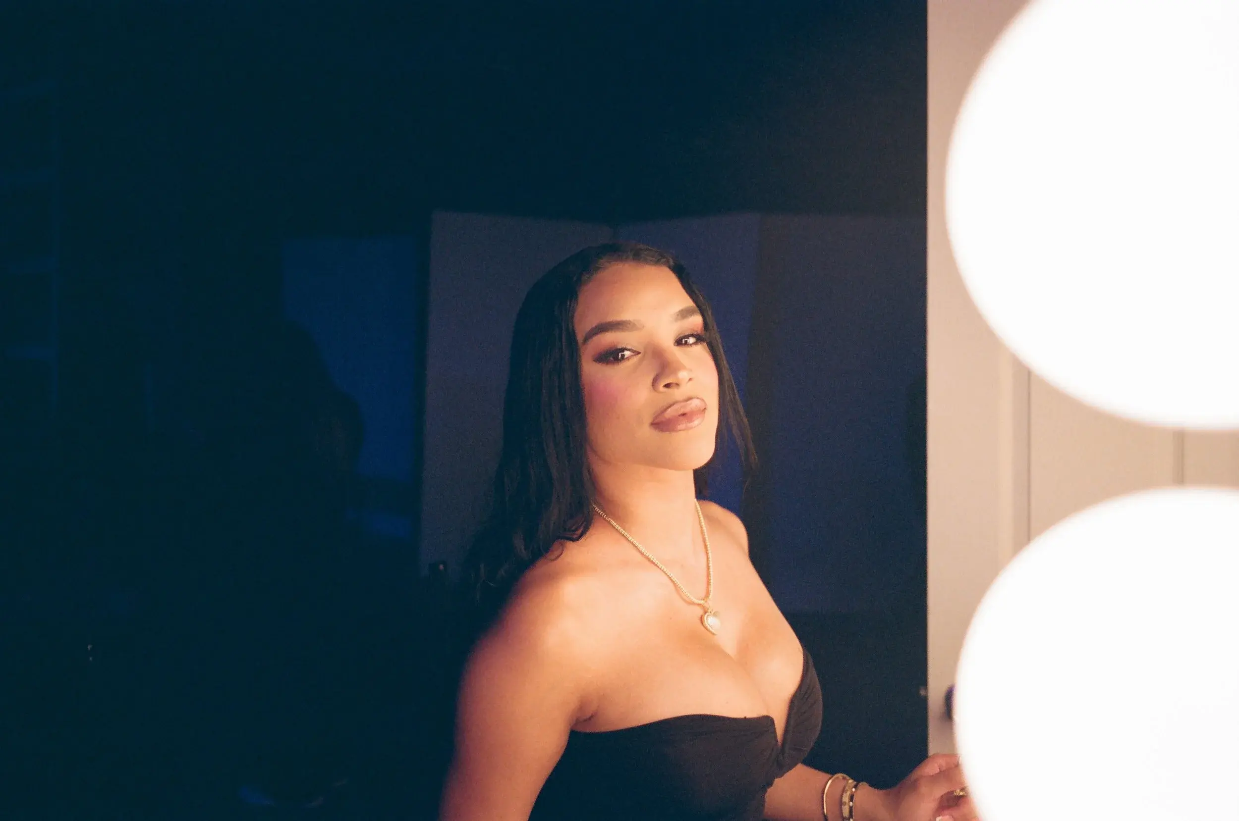 Woman in a black strapless top lit warmly by round globe lamps in darkness