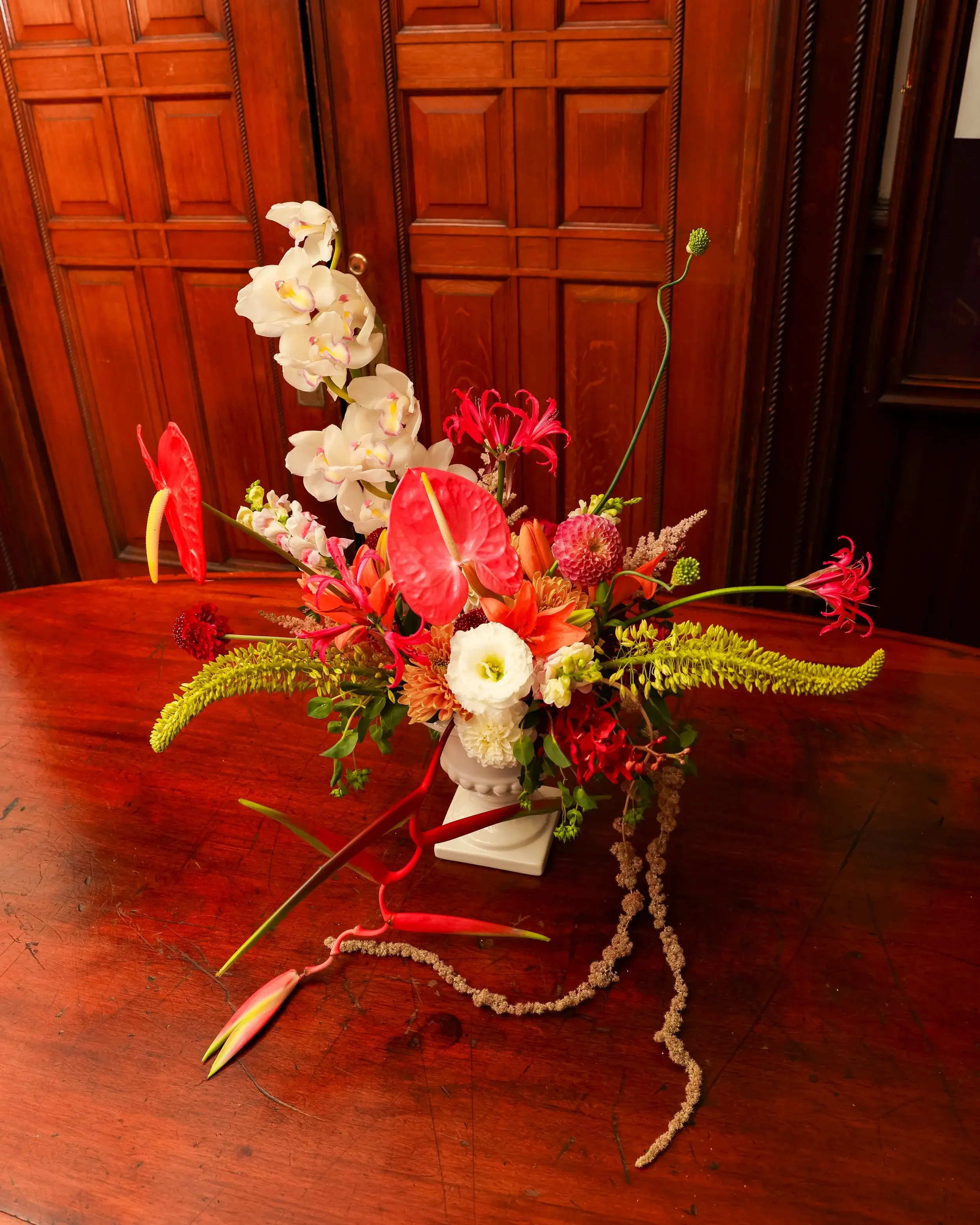 Lush arrangement of orchids, anthuriums, and trailing blooms on a polished wooden table