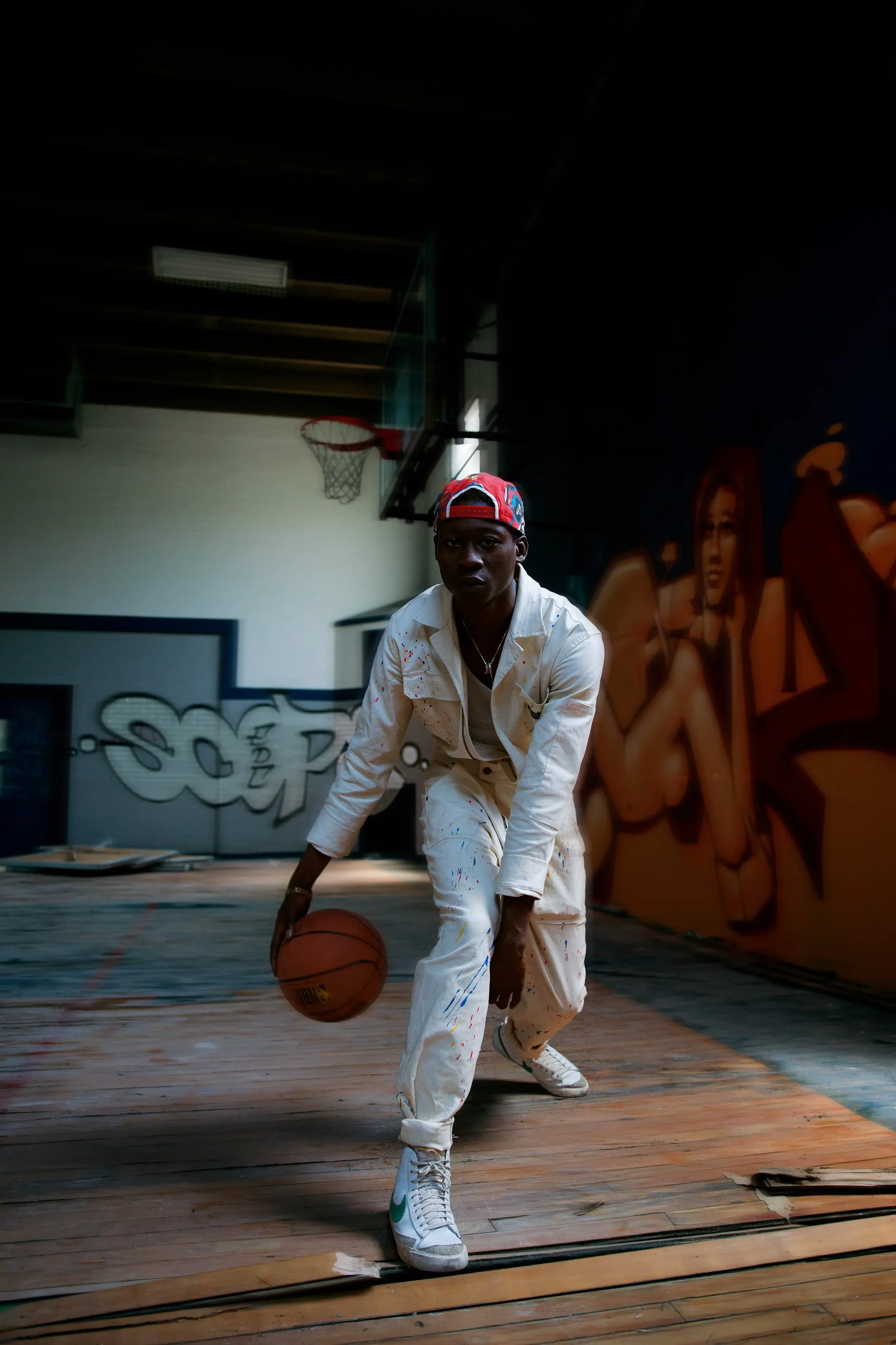 Model in a streetwear cap and white jacket dribbling low beneath the hoop