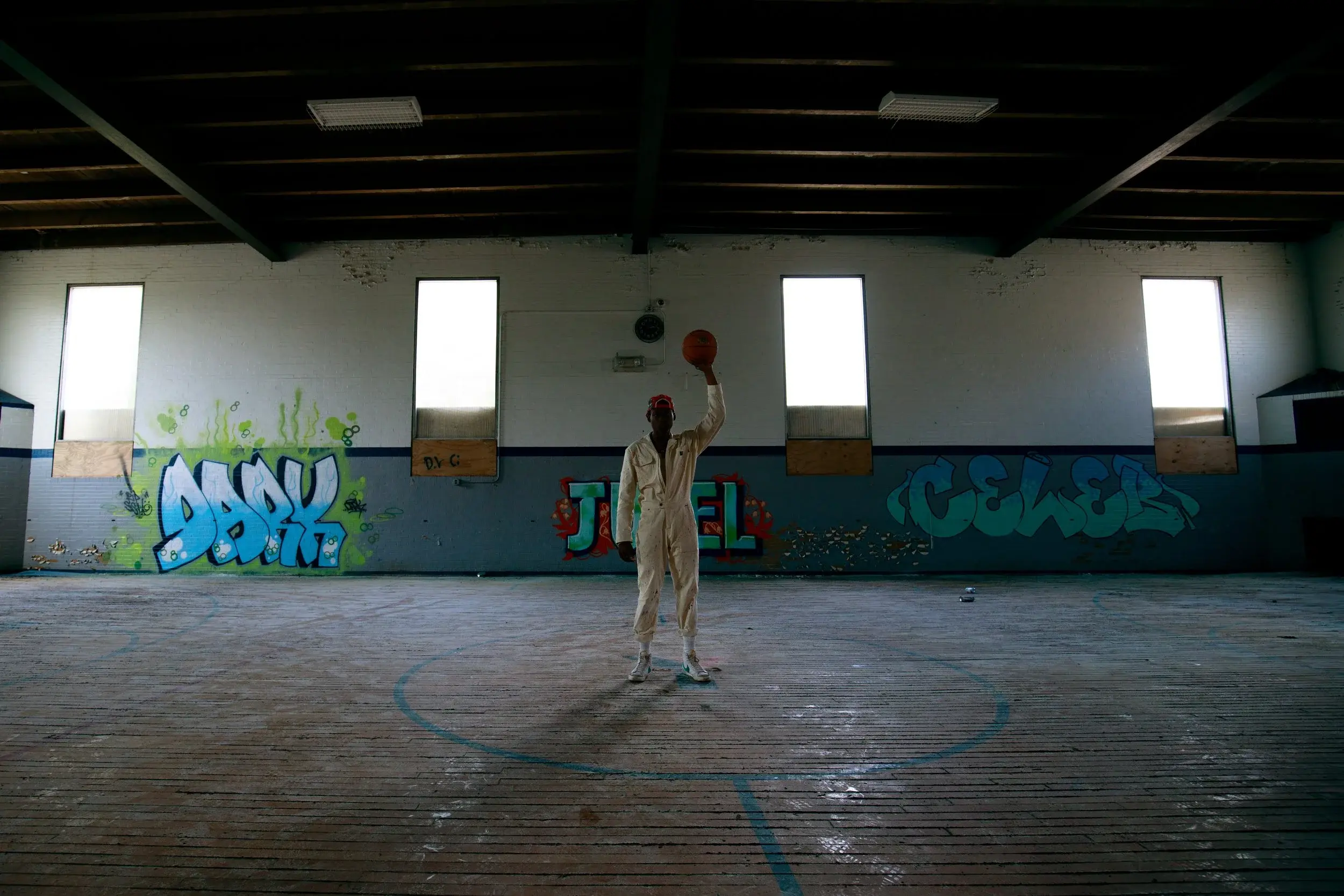 Model raising a basketball overhead at center court of a wide graffiti-walled gym