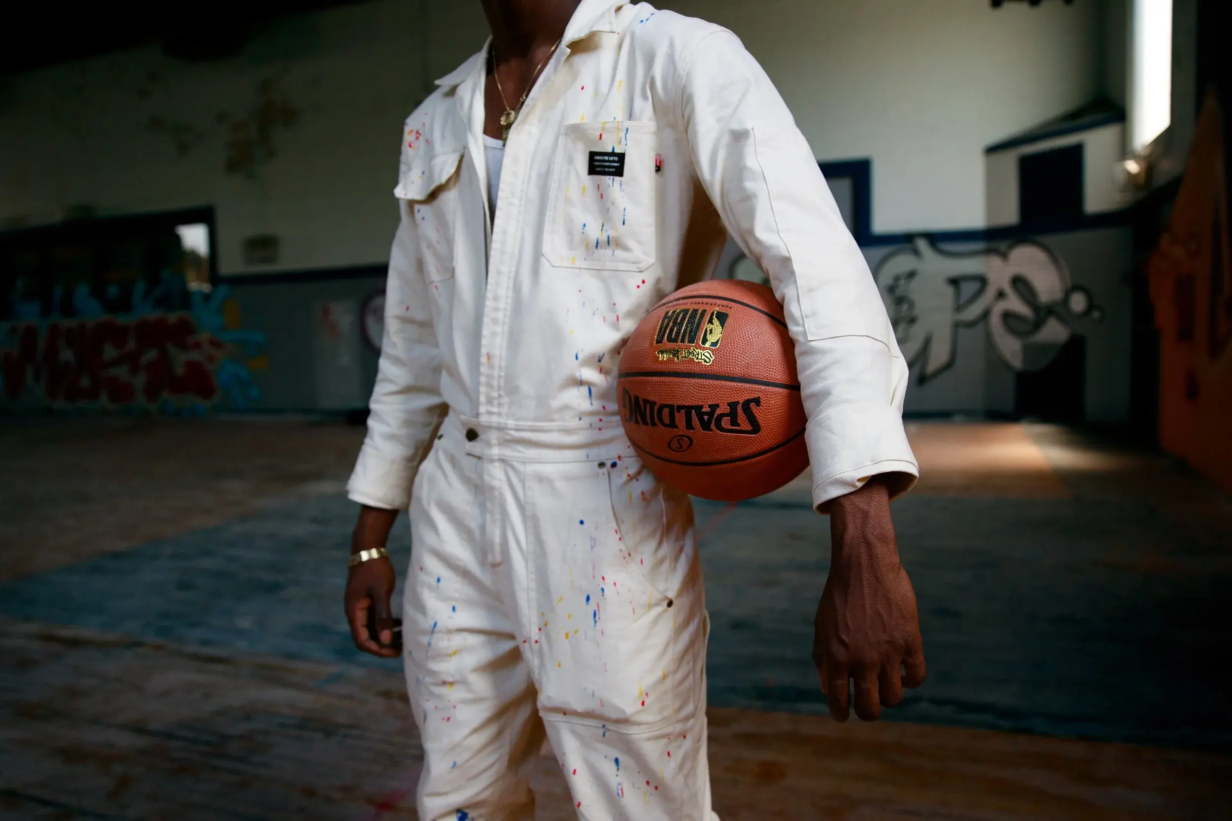 Product detail of a paint-splattered white coverall, model carrying a basketball under one arm