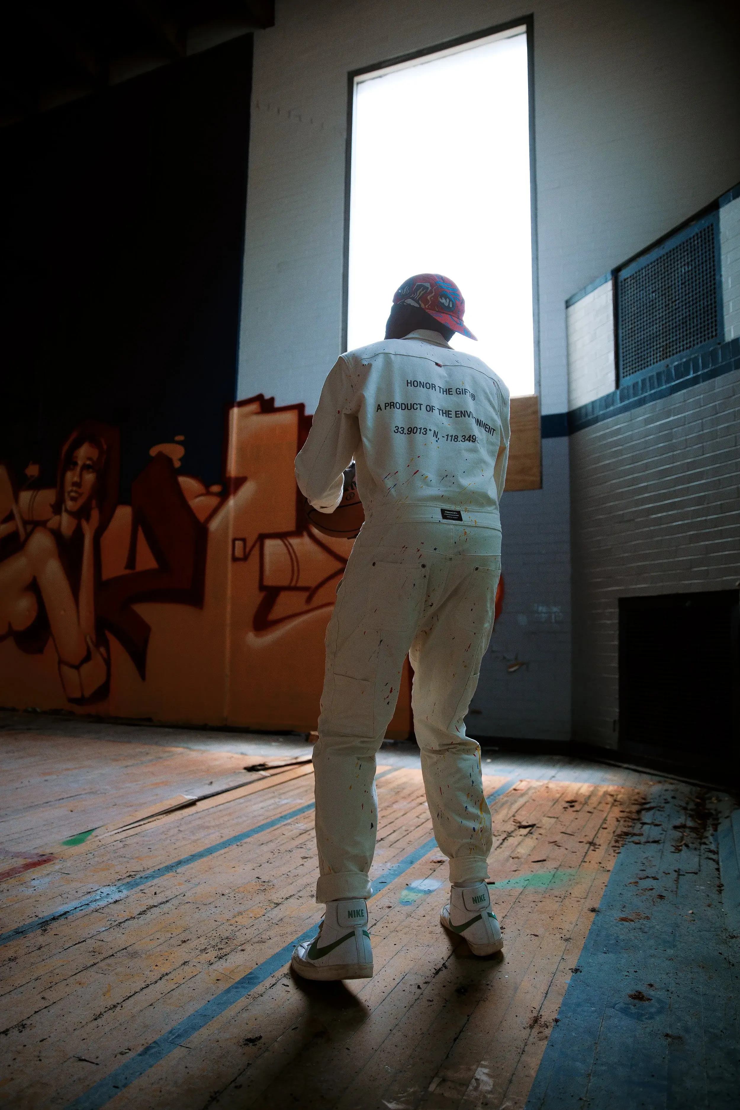 Rear view of a model in a white coverall walking toward a tall bright window