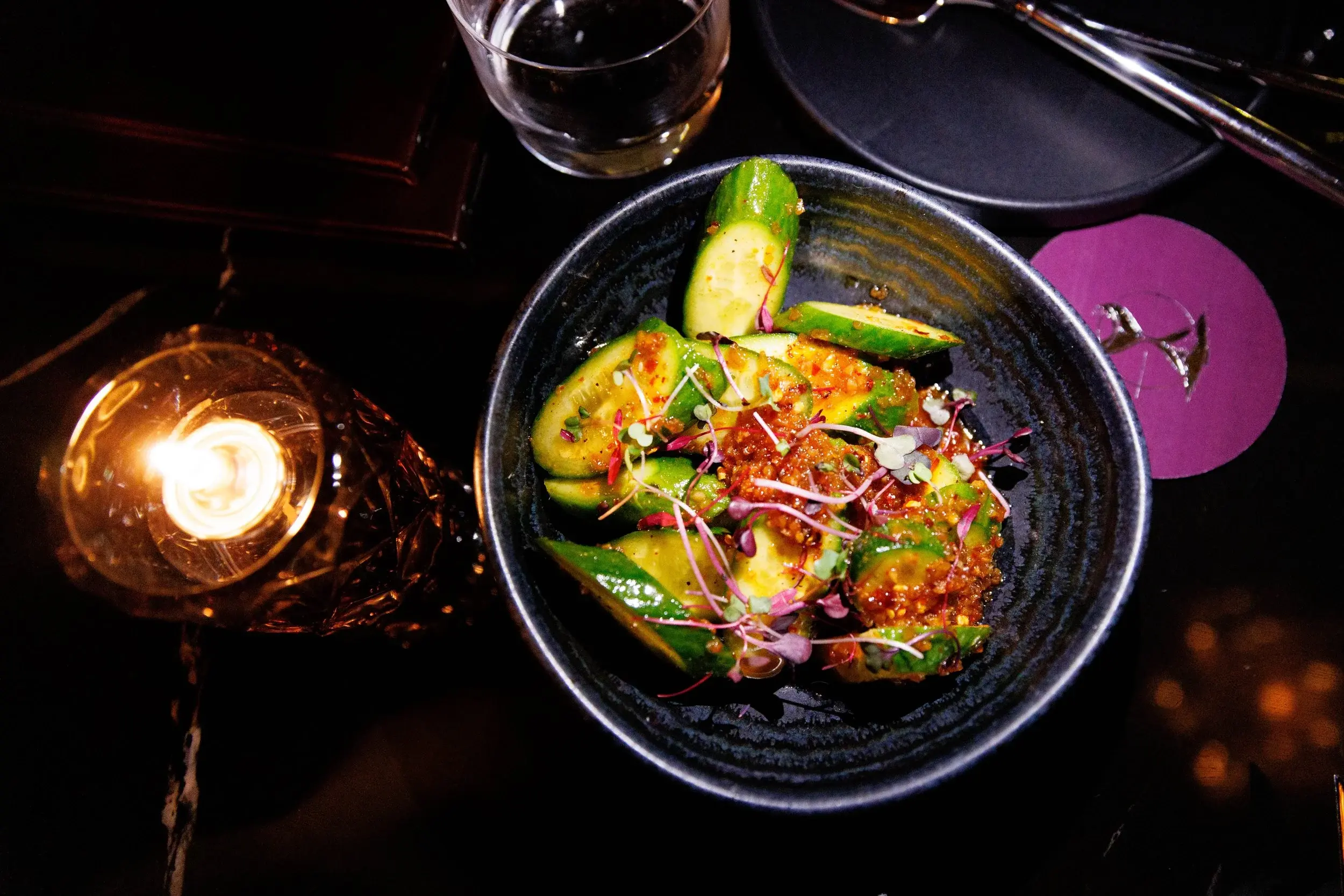 Overhead view of a cucumber salad with chili dressing and microgreens in a dark bowl