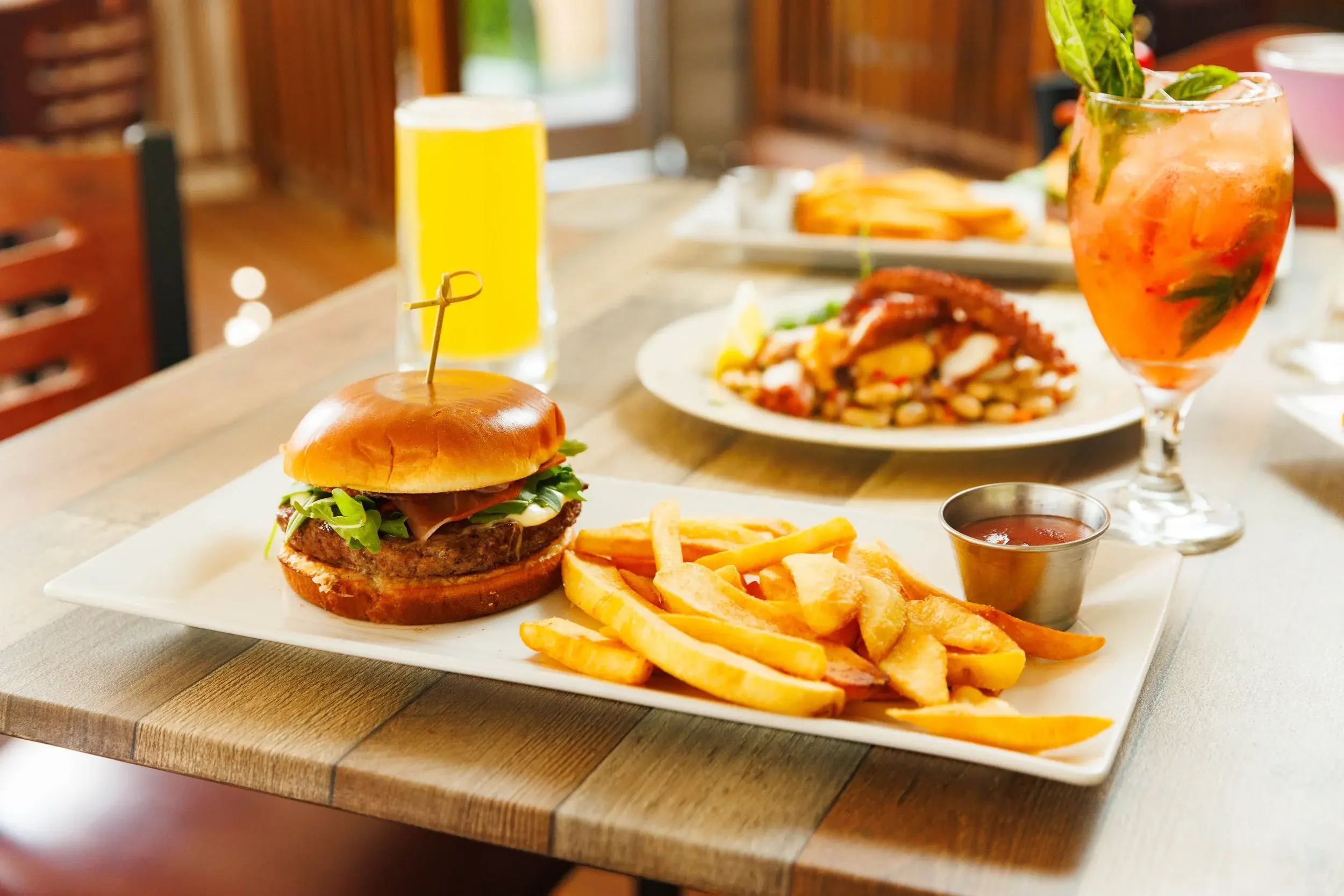Burger with thick-cut fries plated on a long white platter beside a beer