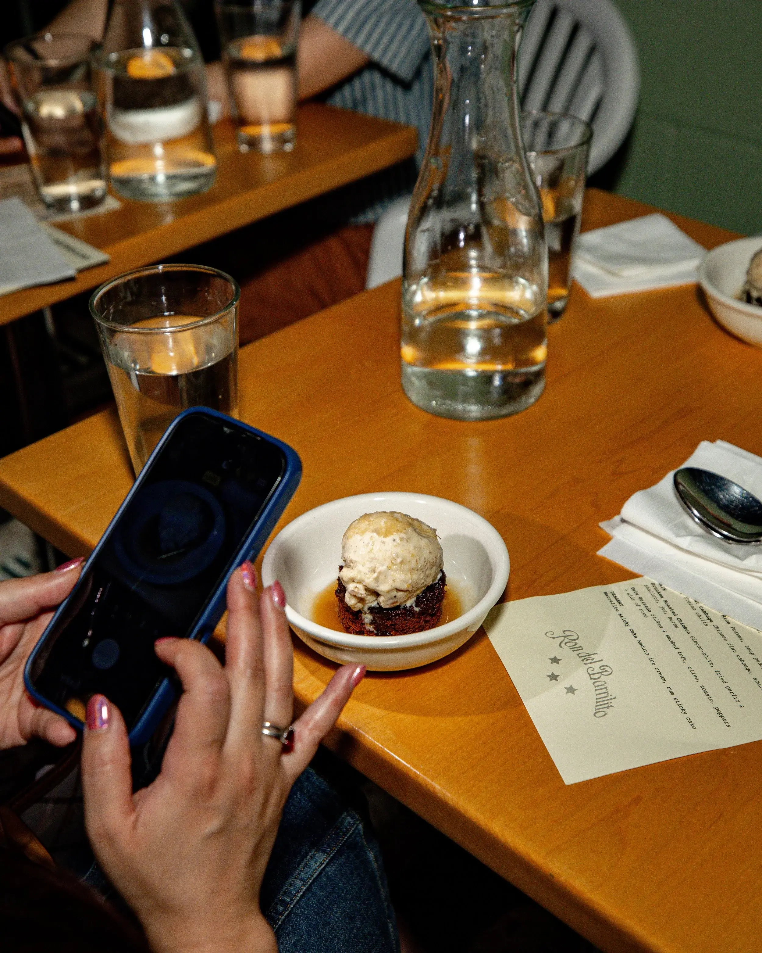 Diner photographing a small dish of ice cream with a phone at a restaurant table