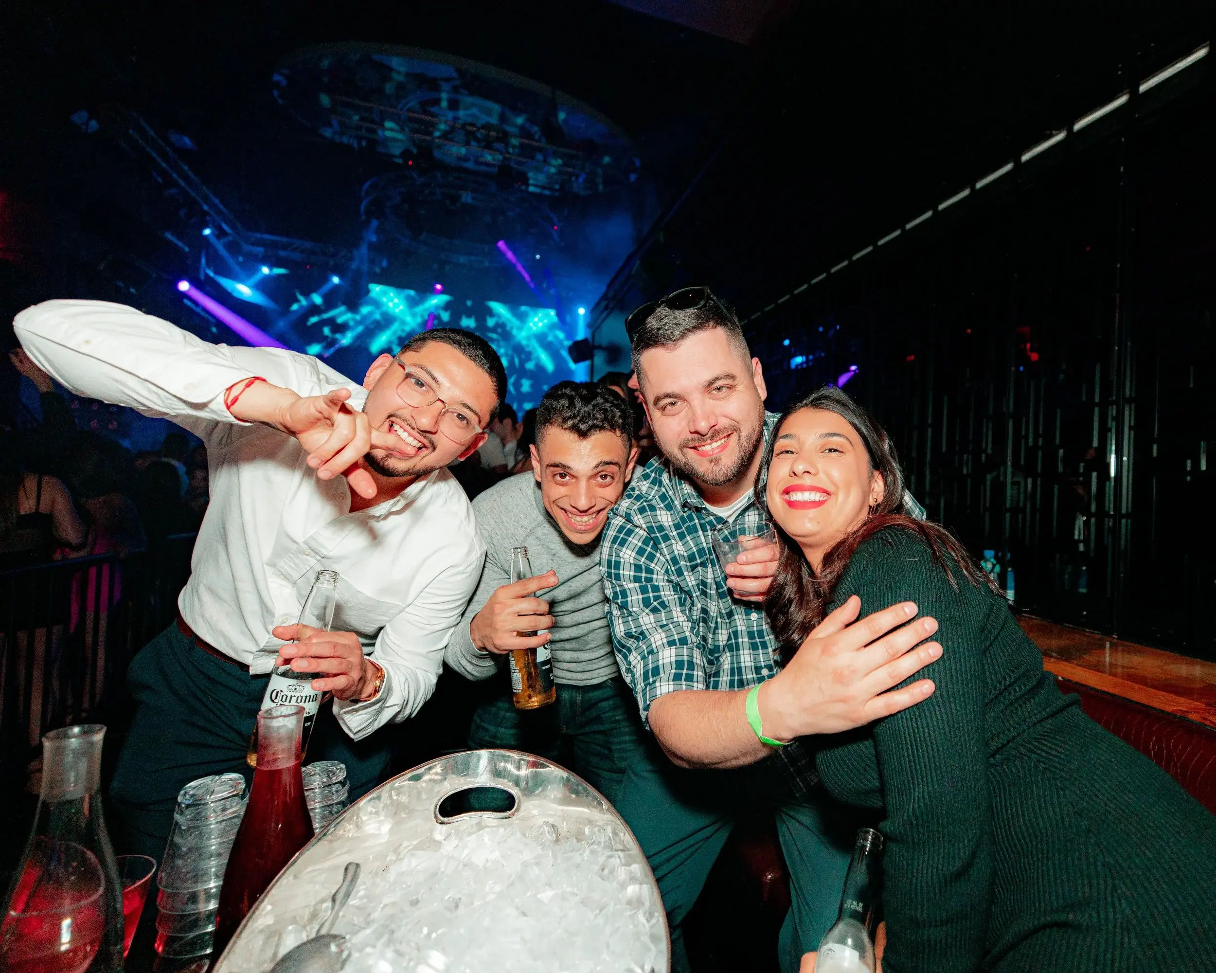 Four friends embracing around an ice bucket as stage lights glow across the club