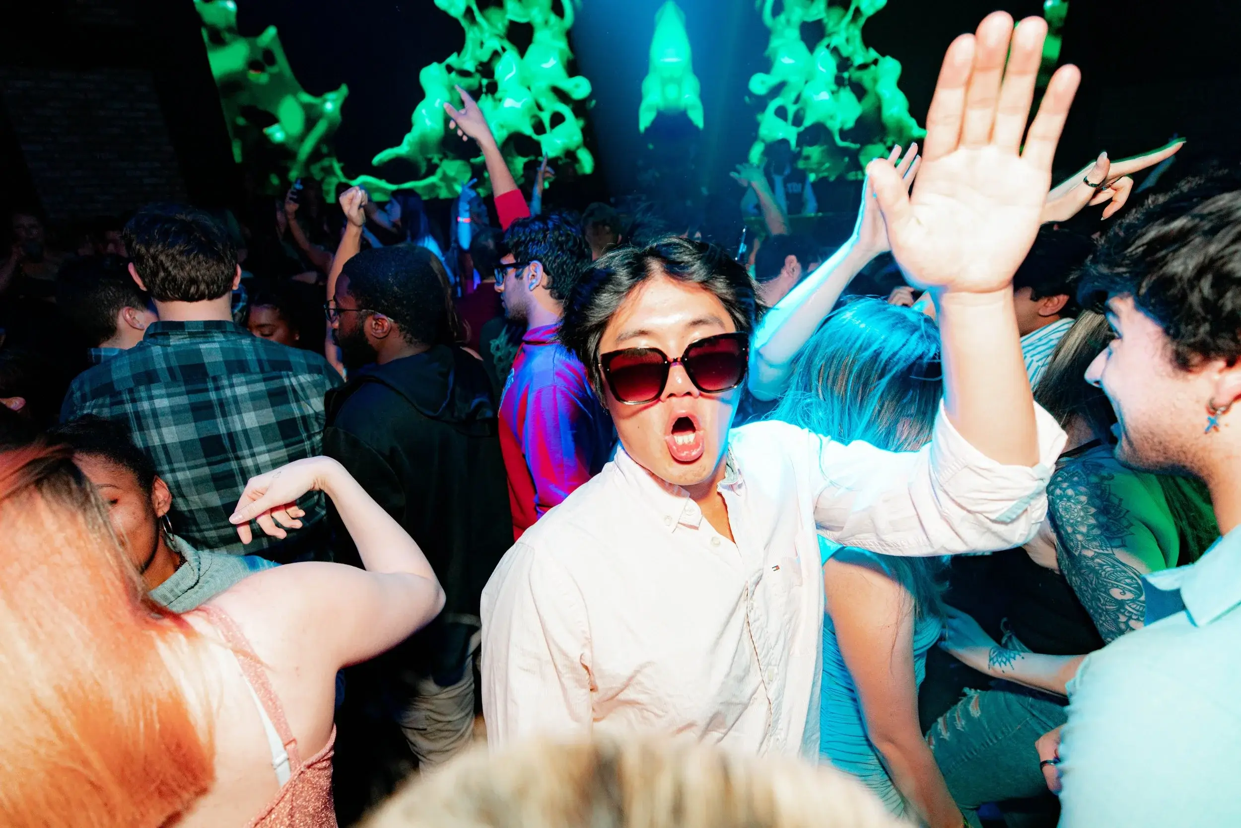 Man in sunglasses shouting with excitement among dancers under green lights