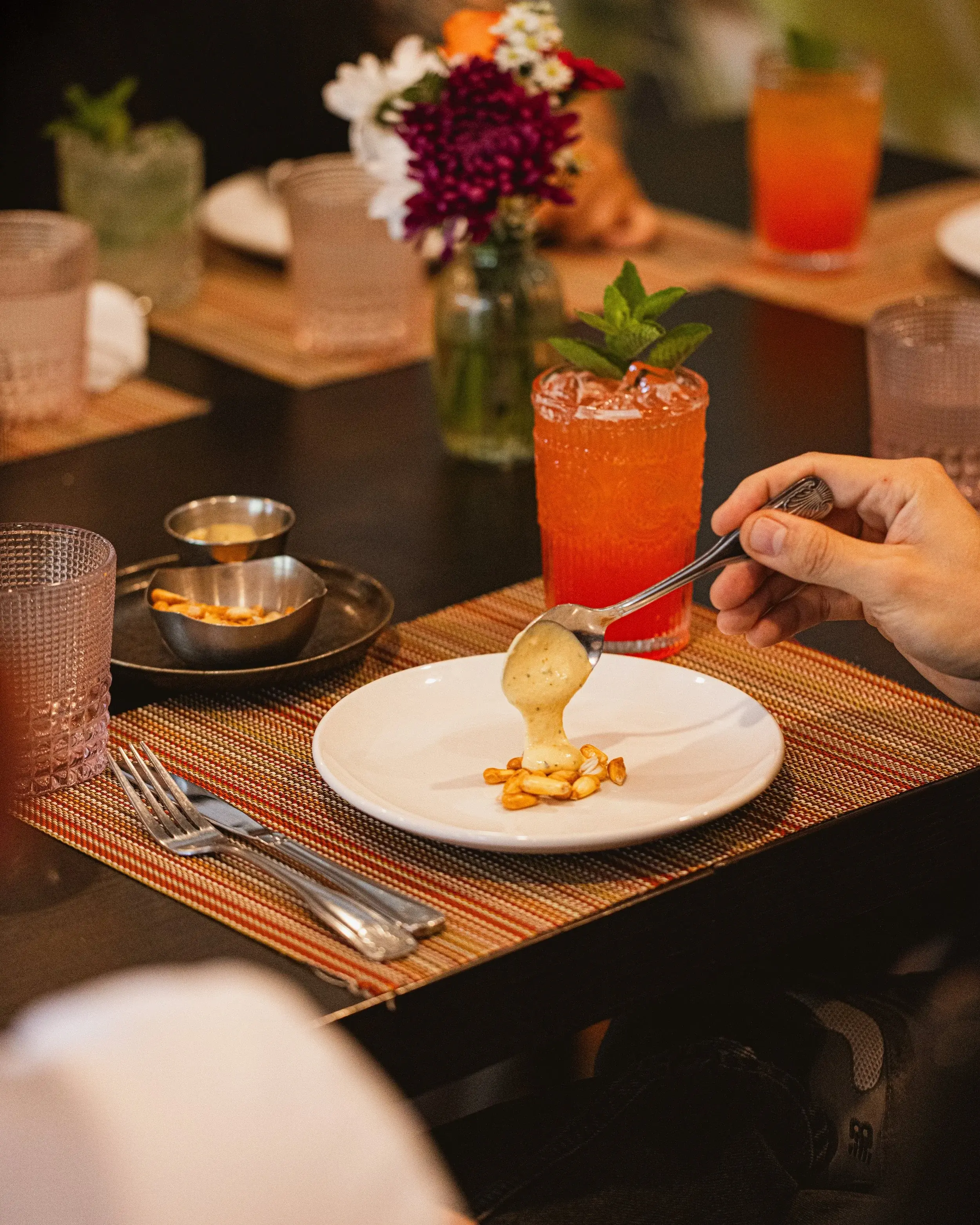 Hand spooning creamy sauce onto a small plate at a set dining table