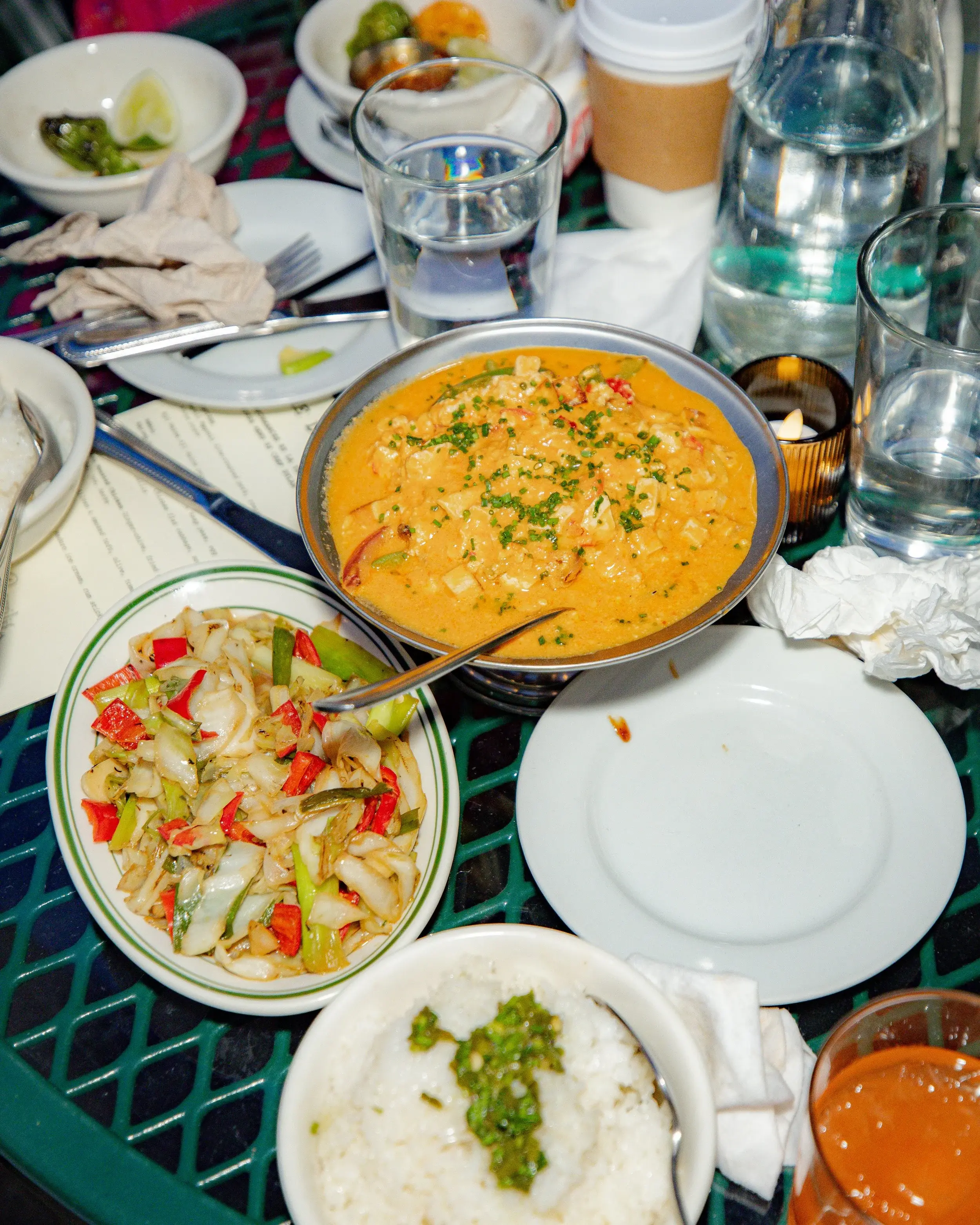 Overhead spread of creamy curry, stir-fried vegetables, and rice crowding a restaurant table