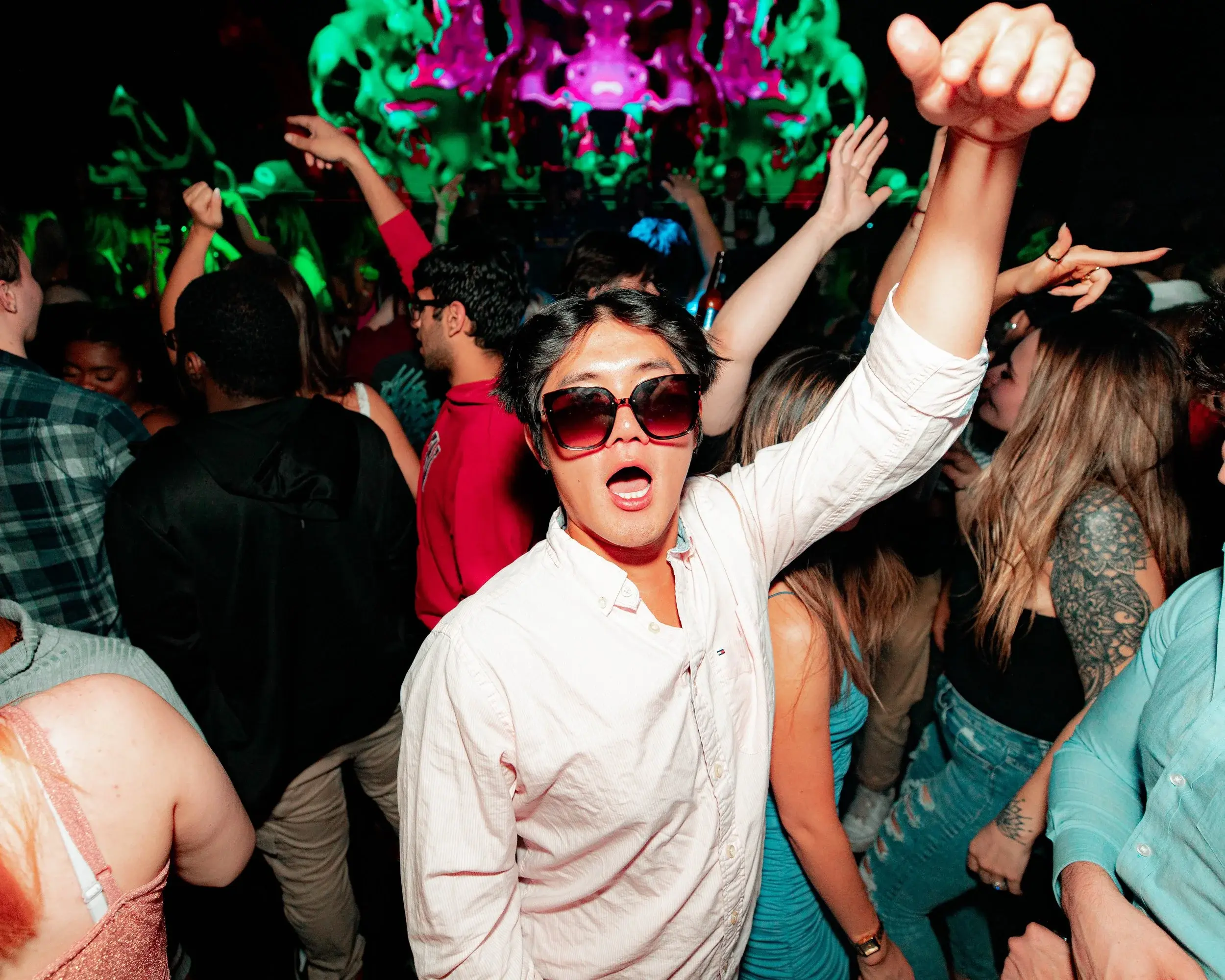 Dancer in a white shirt raising his fist as neon lights wash over the nightlife crowd