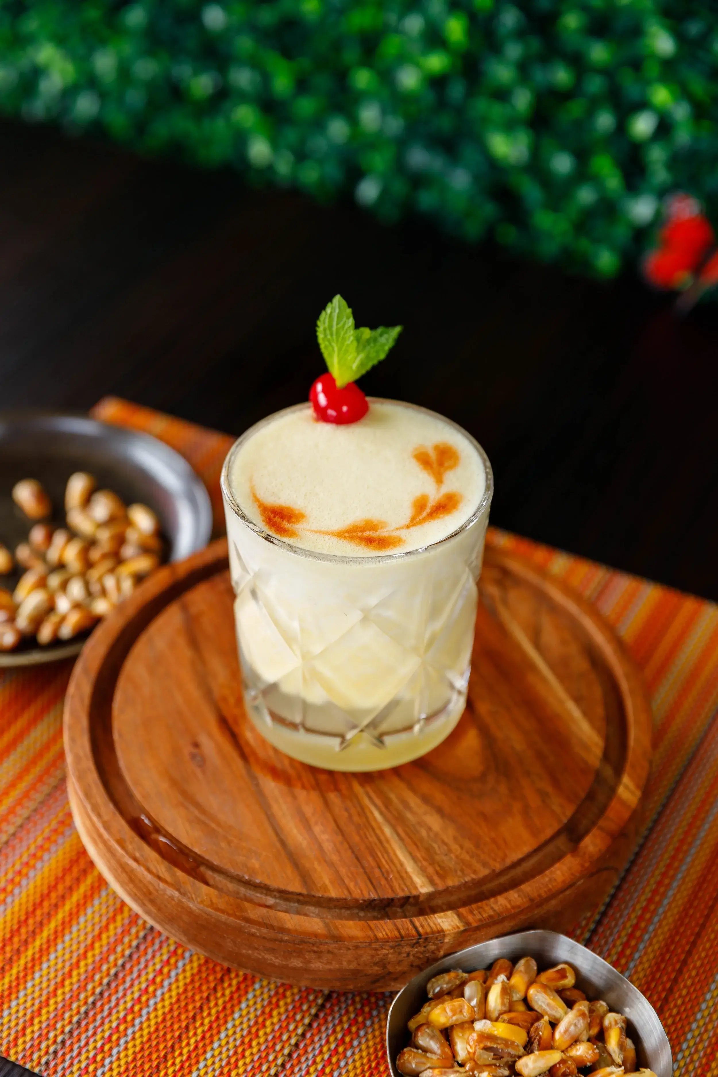 Foam-topped sour cocktail with mint and a cherry on a round wooden board