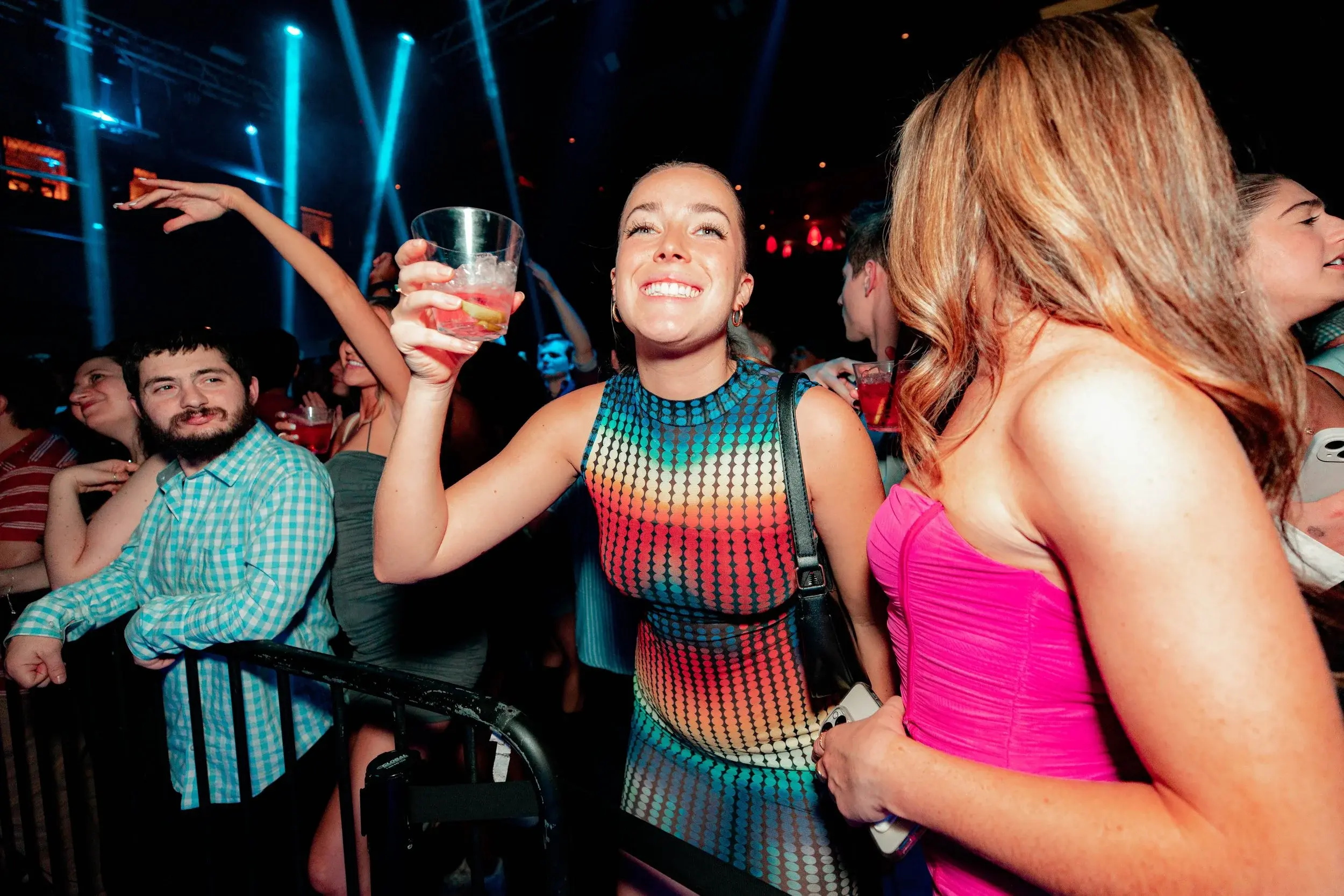 Smiling woman in a rainbow-patterned dress lifting her cocktail on the dance floor