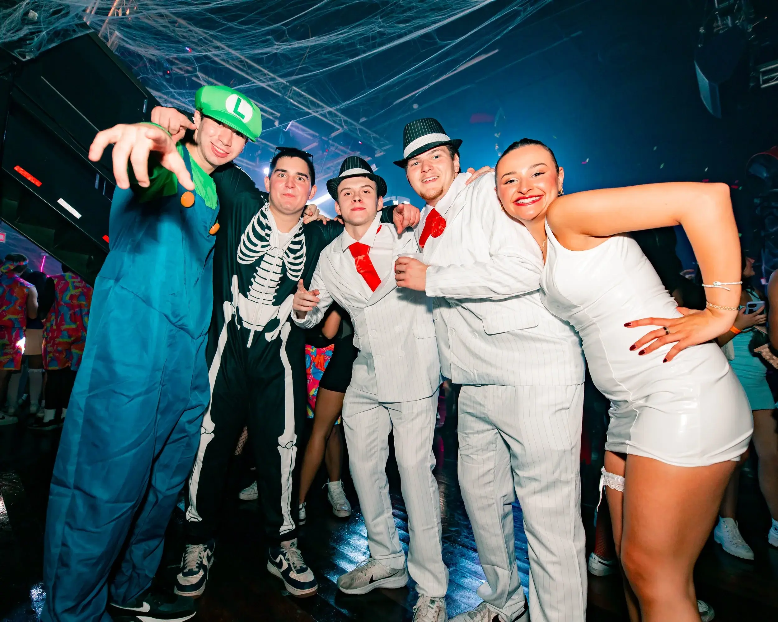 Five costumed friends posing under fake cobwebs during a themed club night