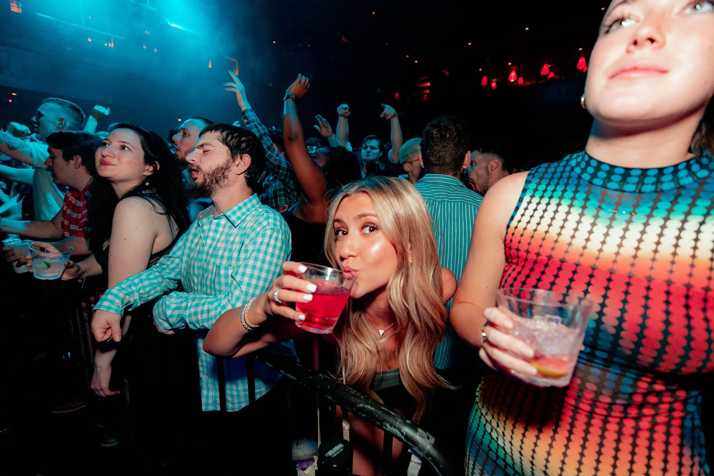 Woman sipping a red cocktail at the rail while the crowd dances behind her