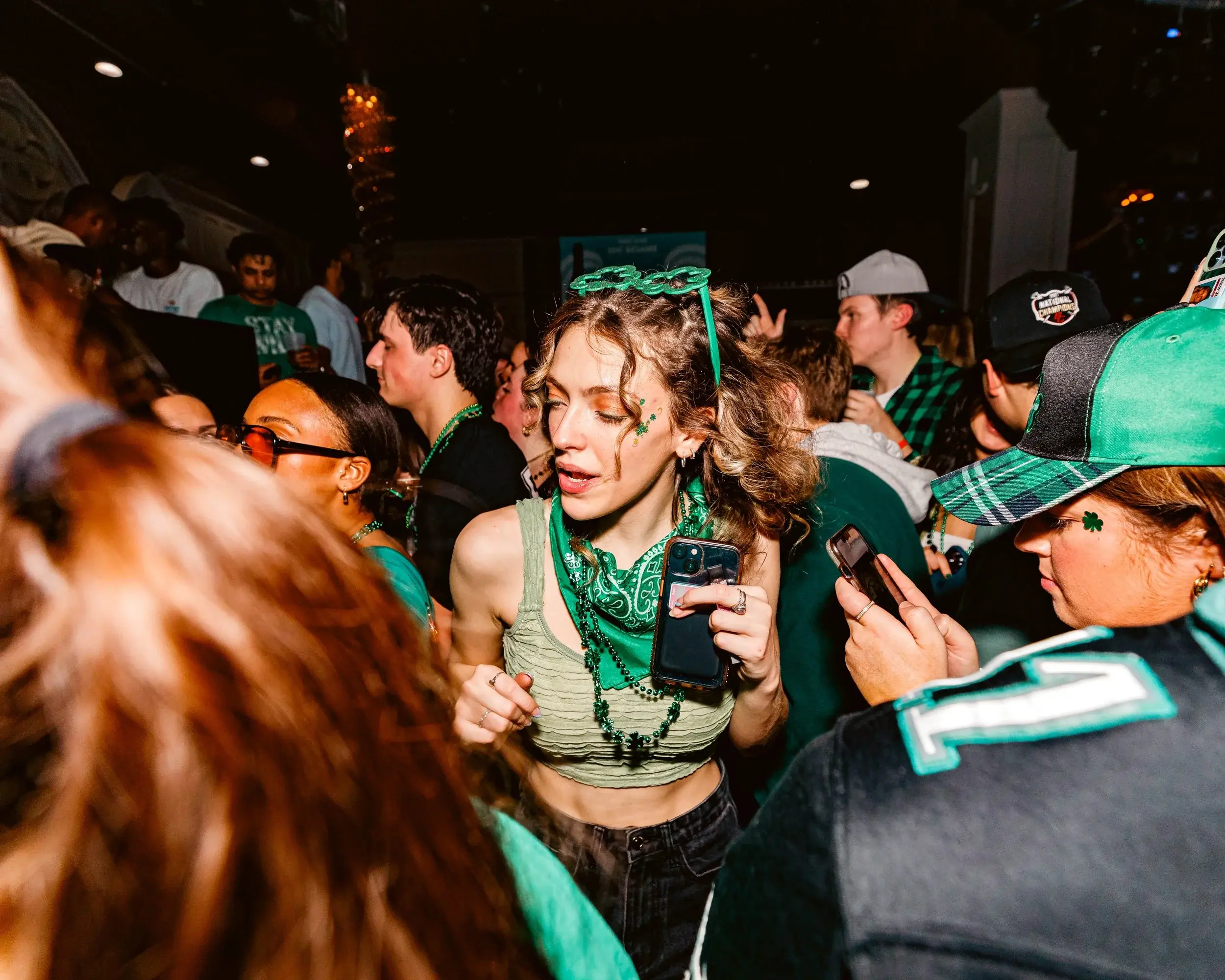 Woman with a green bandana dancing through a crowded bar celebration