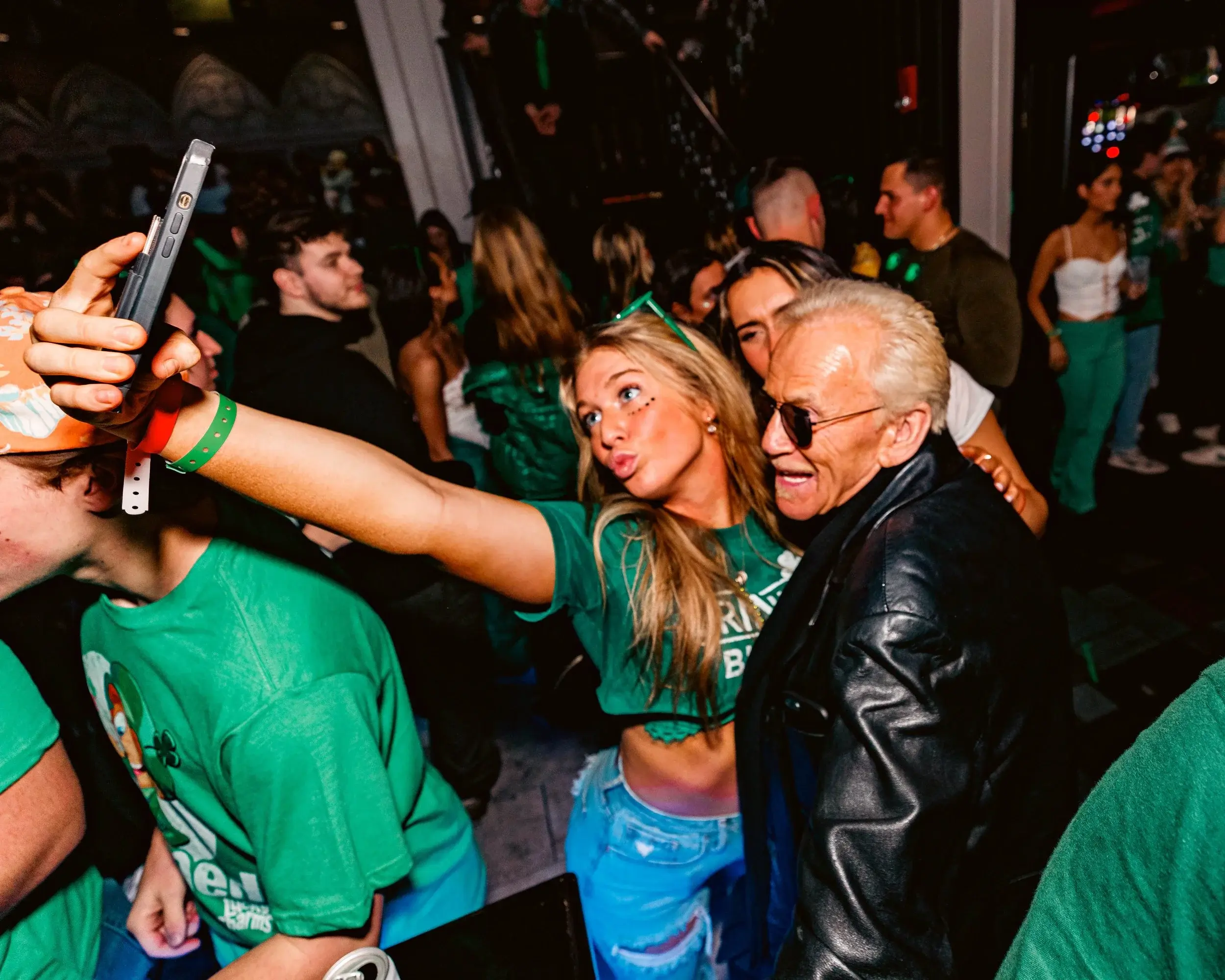 Young woman taking a selfie with an older man in a packed nightlife crowd
