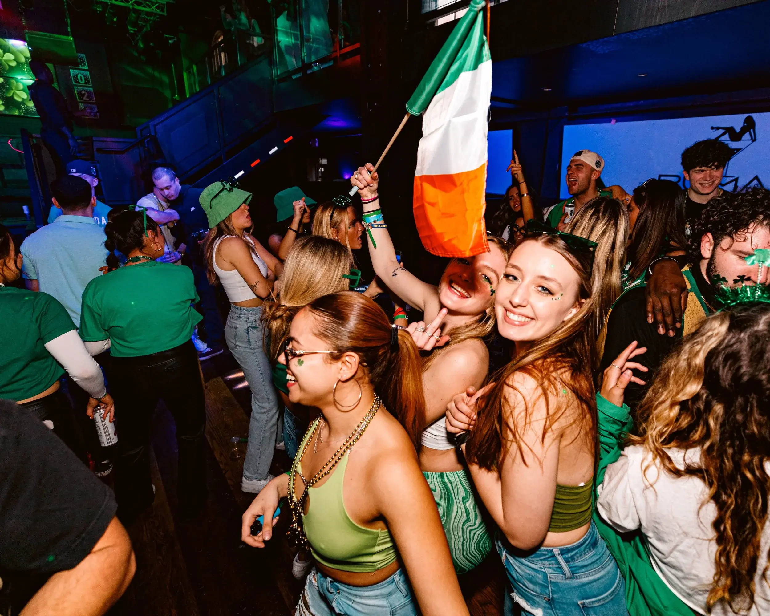 Reveler waving a tricolor flag above friends dancing in a neon-lit club
