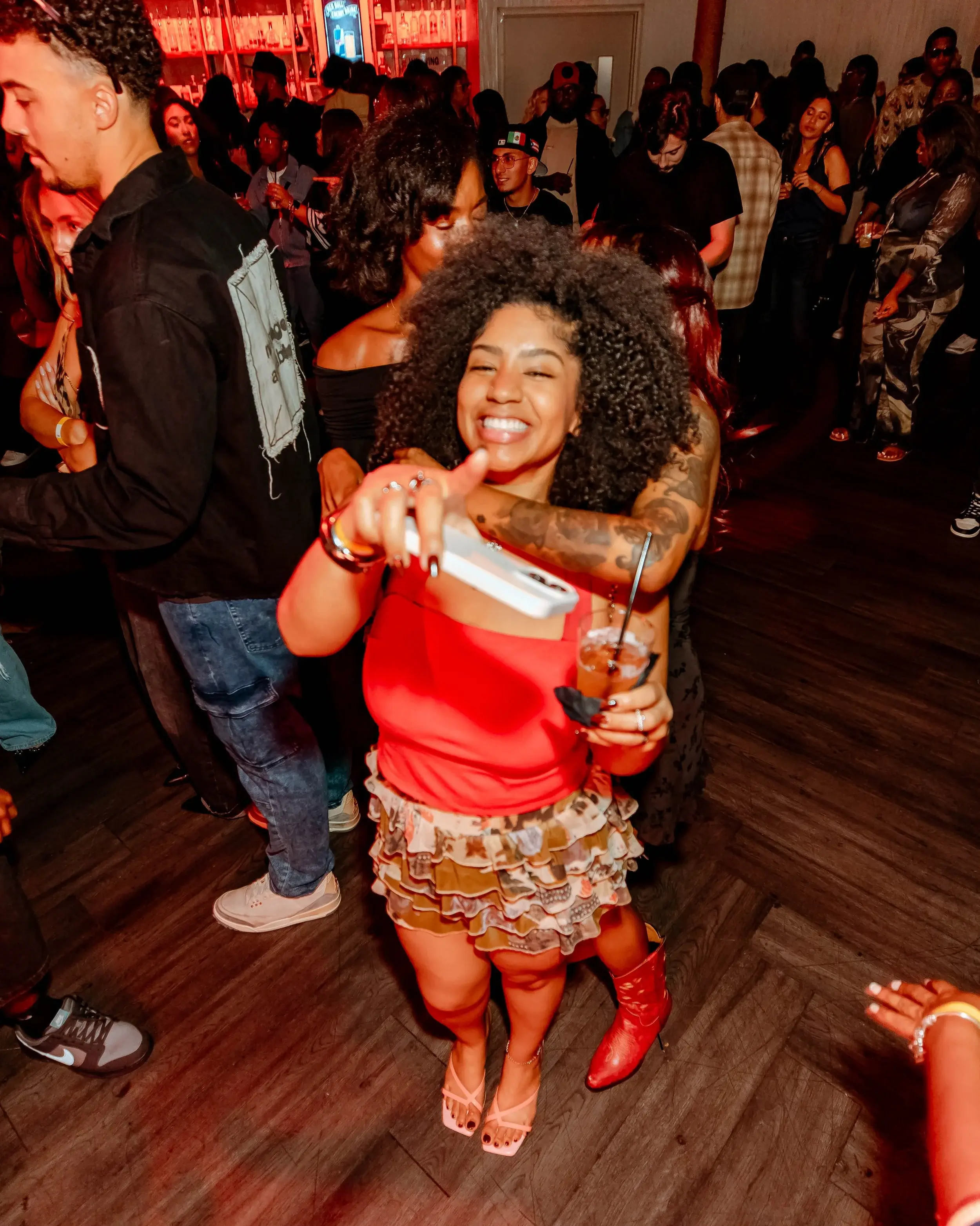 Laughing woman in red dancing with a drink in a warmly lit lounge
