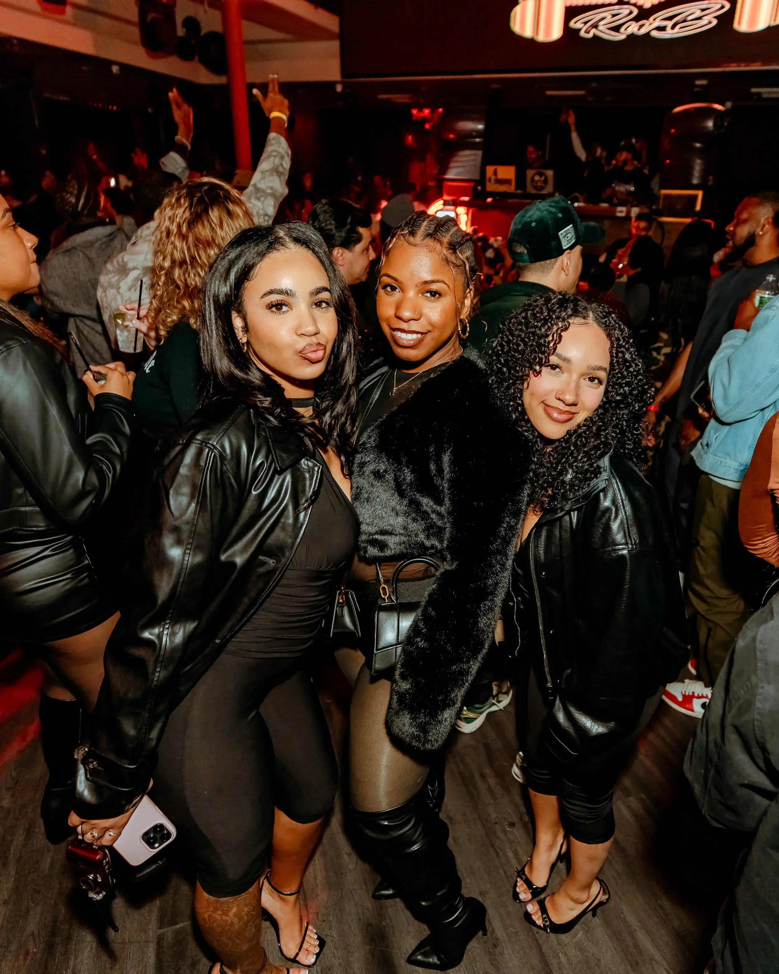 Three friends in leather jackets posing together under red nightlife lighting