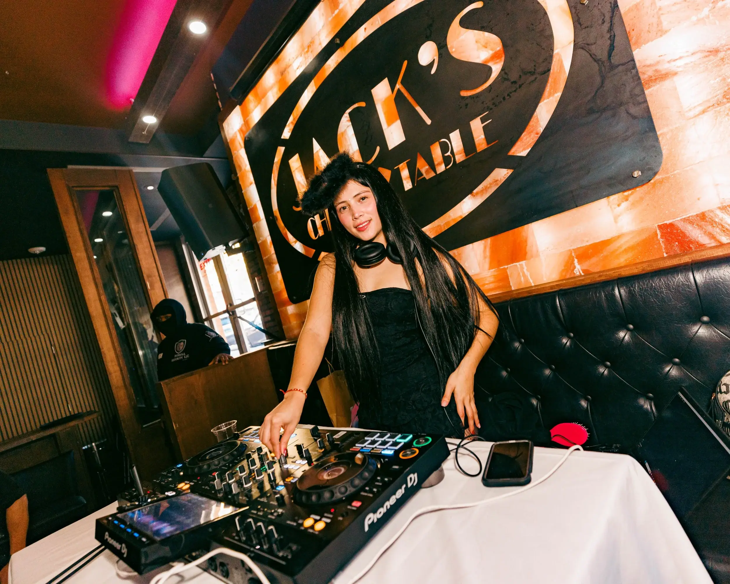 DJ mixing on turntables beside tufted leather booths in a warmly lit venue