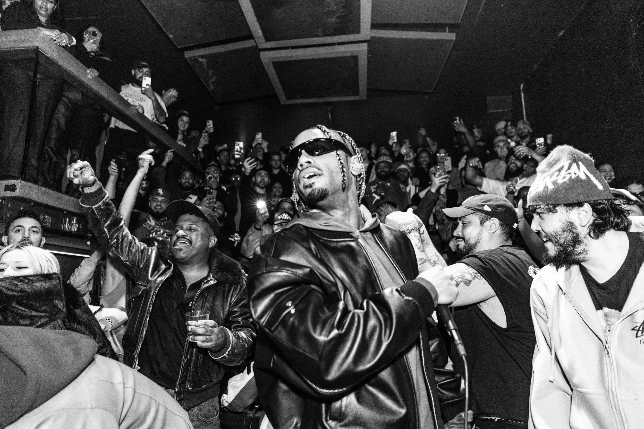 Black and white view of a performer in sunglasses moving through an excited crowd