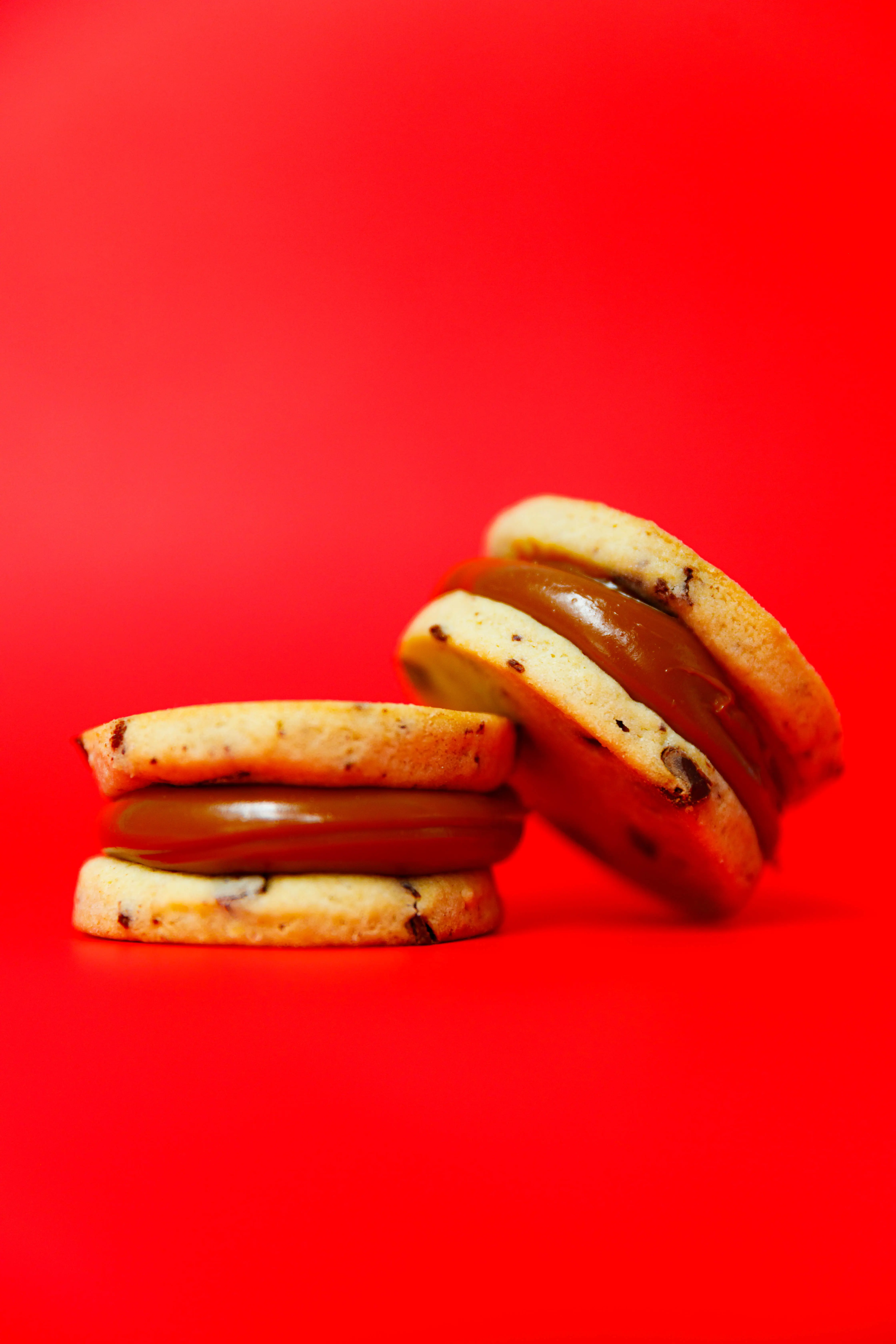 Chocolate-chip alfajores filled with dulce de leche stacked on a red backdrop