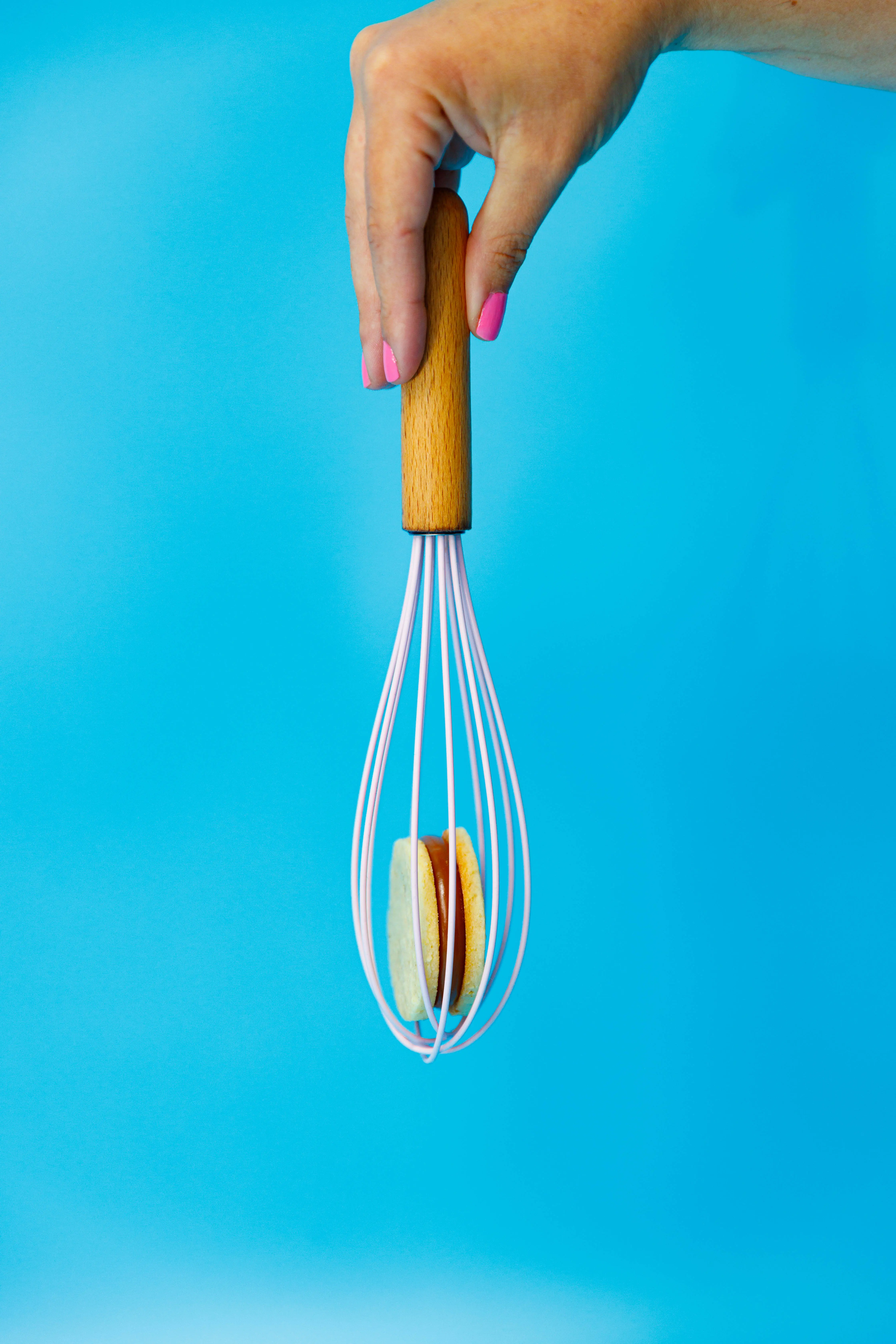 Alfajor cookie balanced in a whisk against a bright blue backdrop