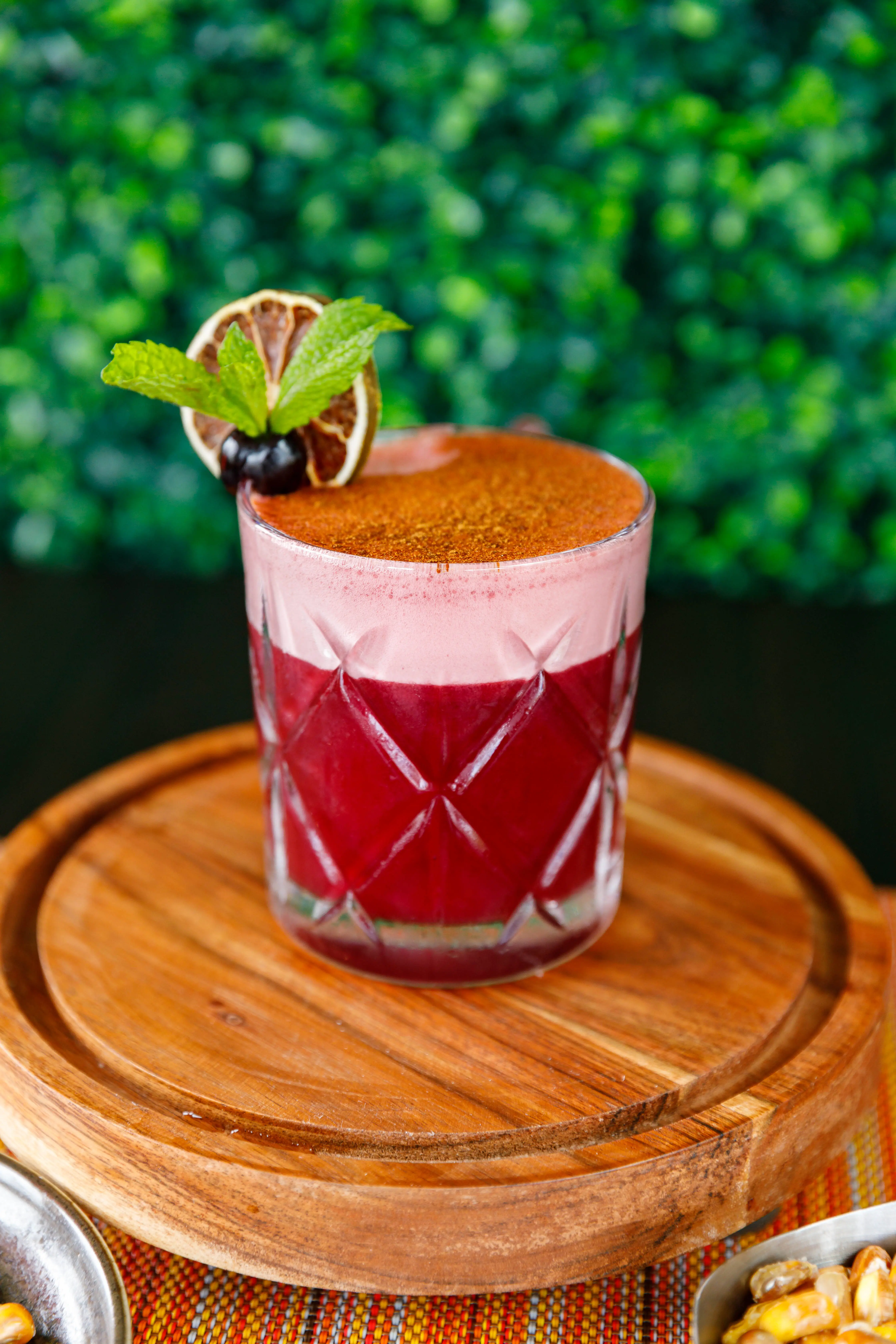 Berry cocktail dusted with spice on a wooden board against greenery