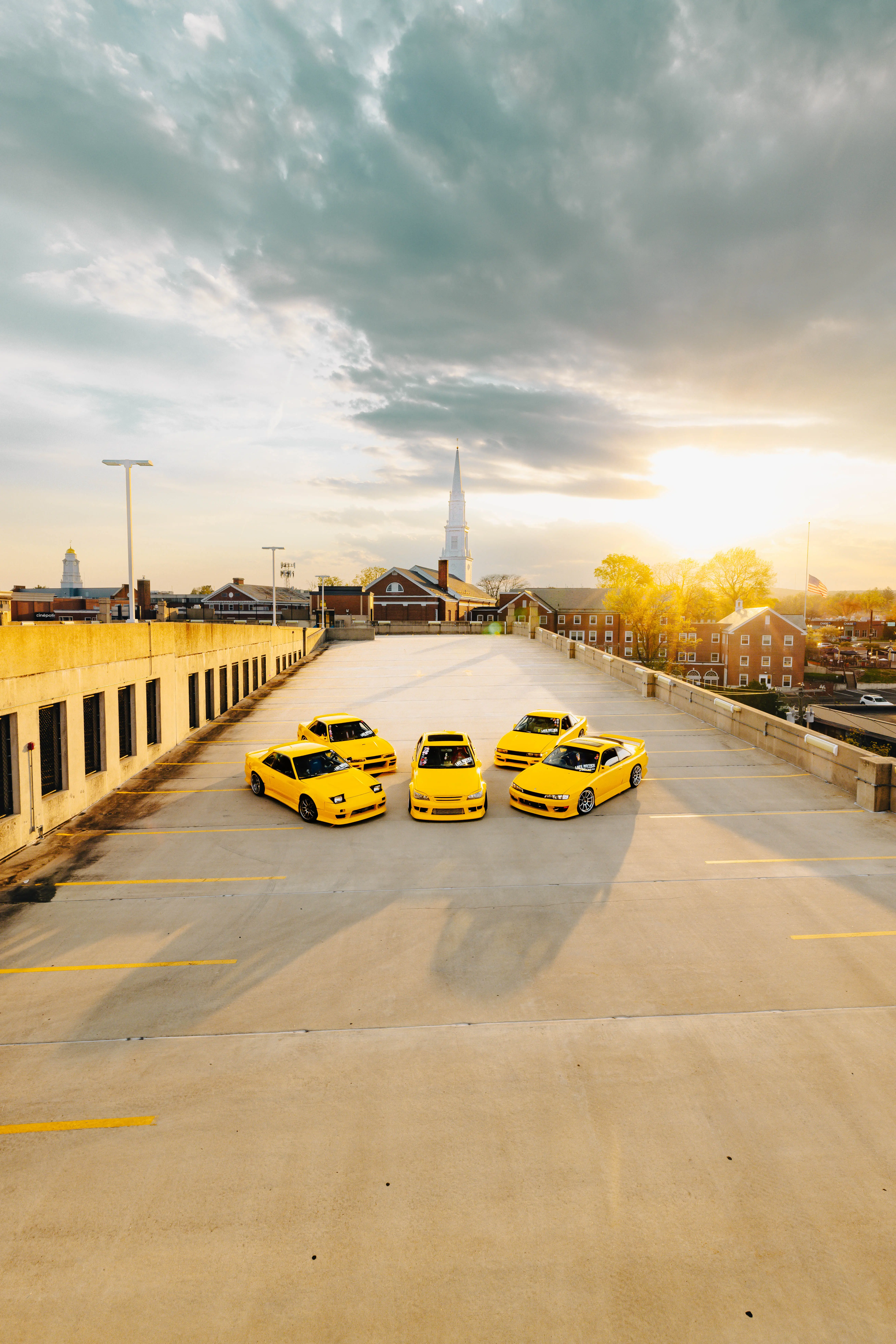 Three yellow sports cars parked on a rooftop deck at golden hour