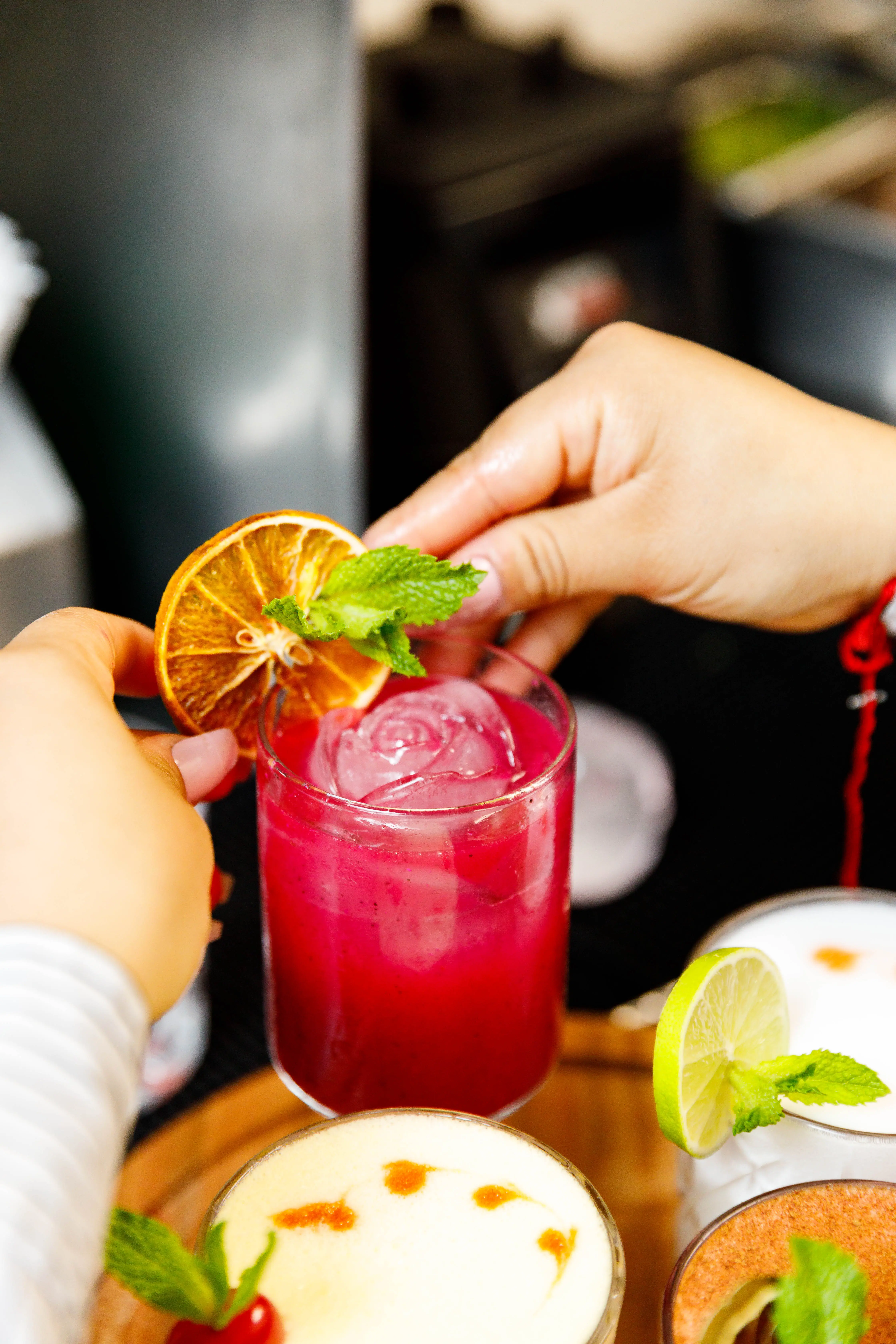 Bartender handing over a red cocktail garnished with dried citrus and mint