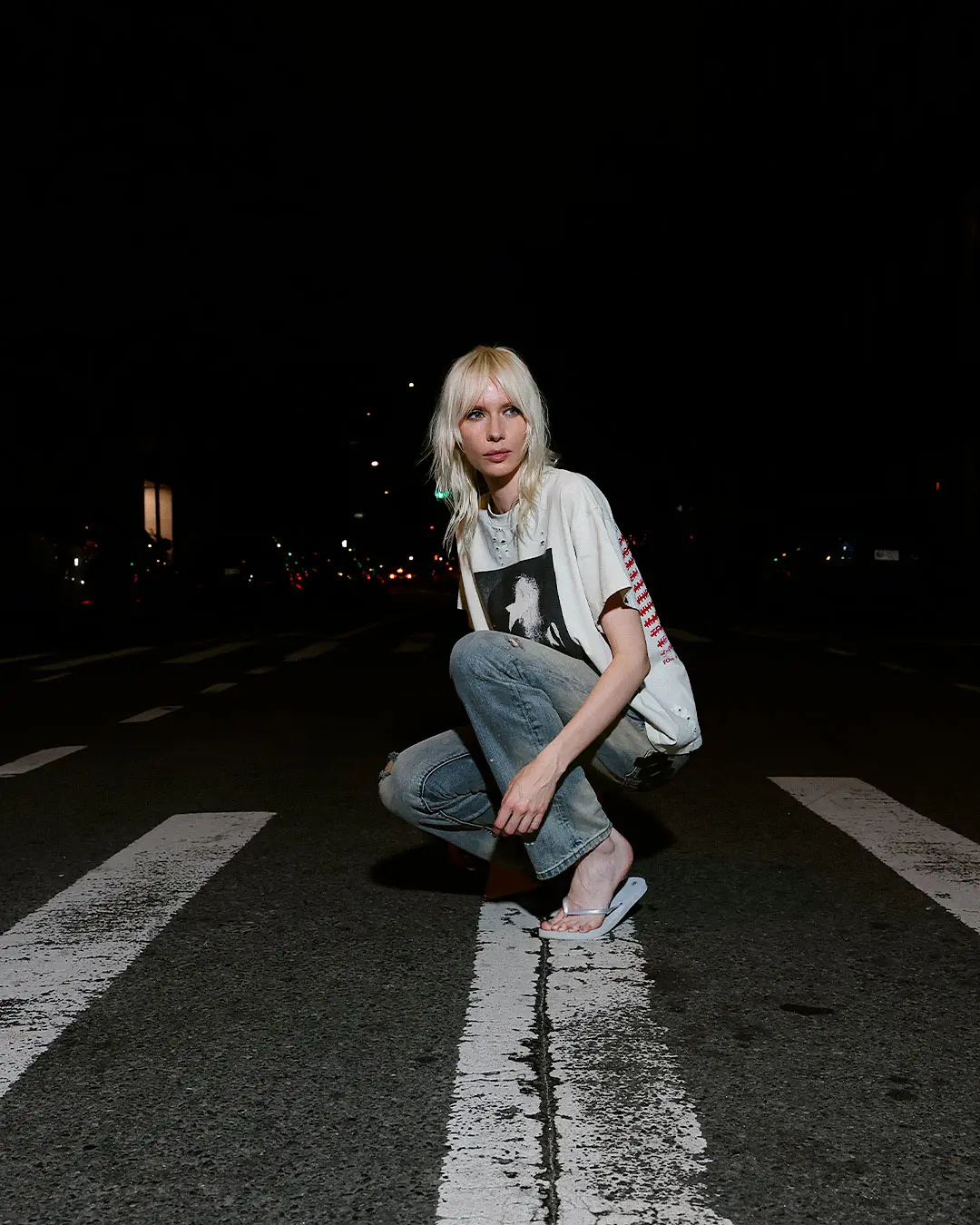 Night portrait of a person crouching on a crosswalk with city lights behind