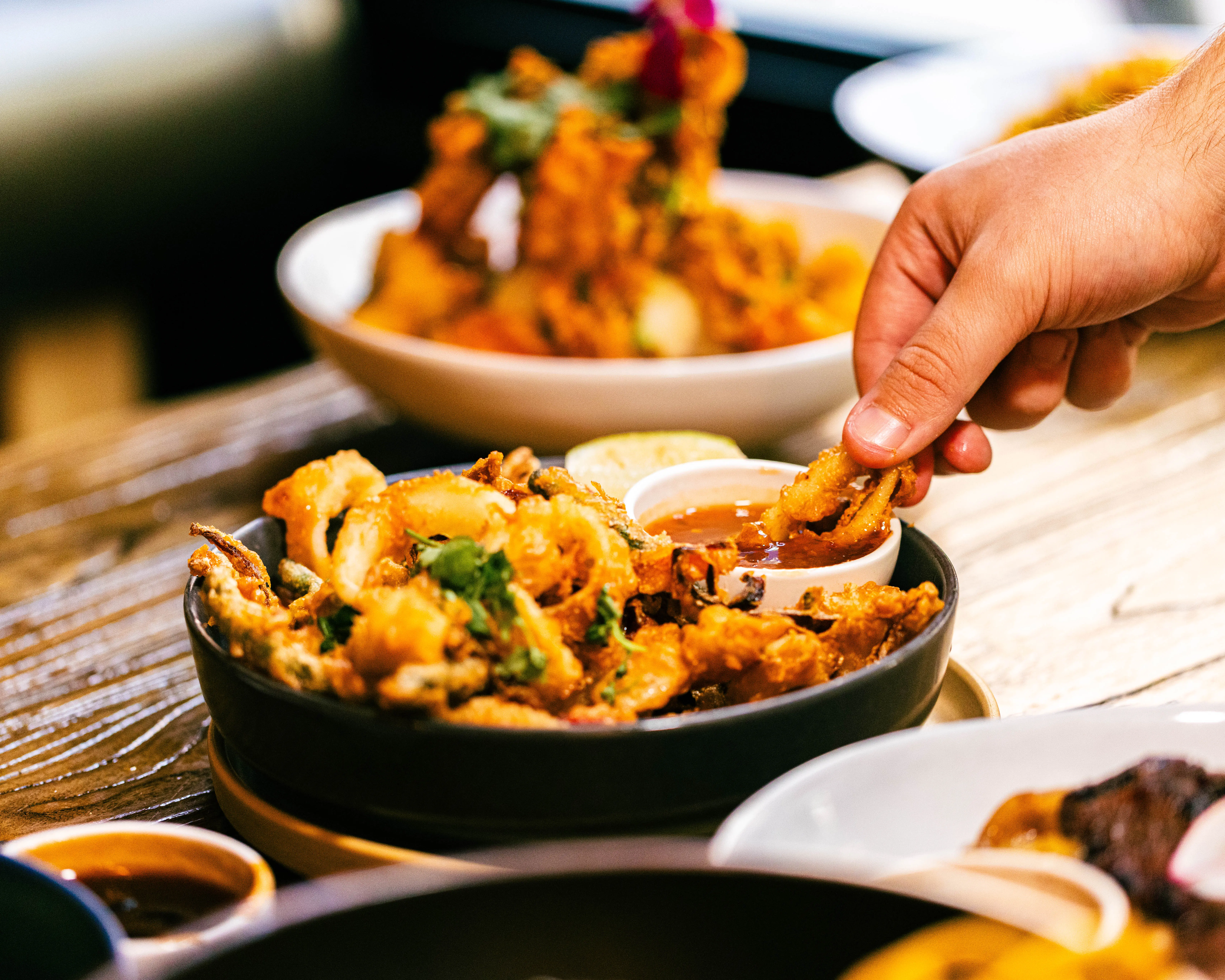 Hands dipping crispy fried bites into sauce over a black bowl