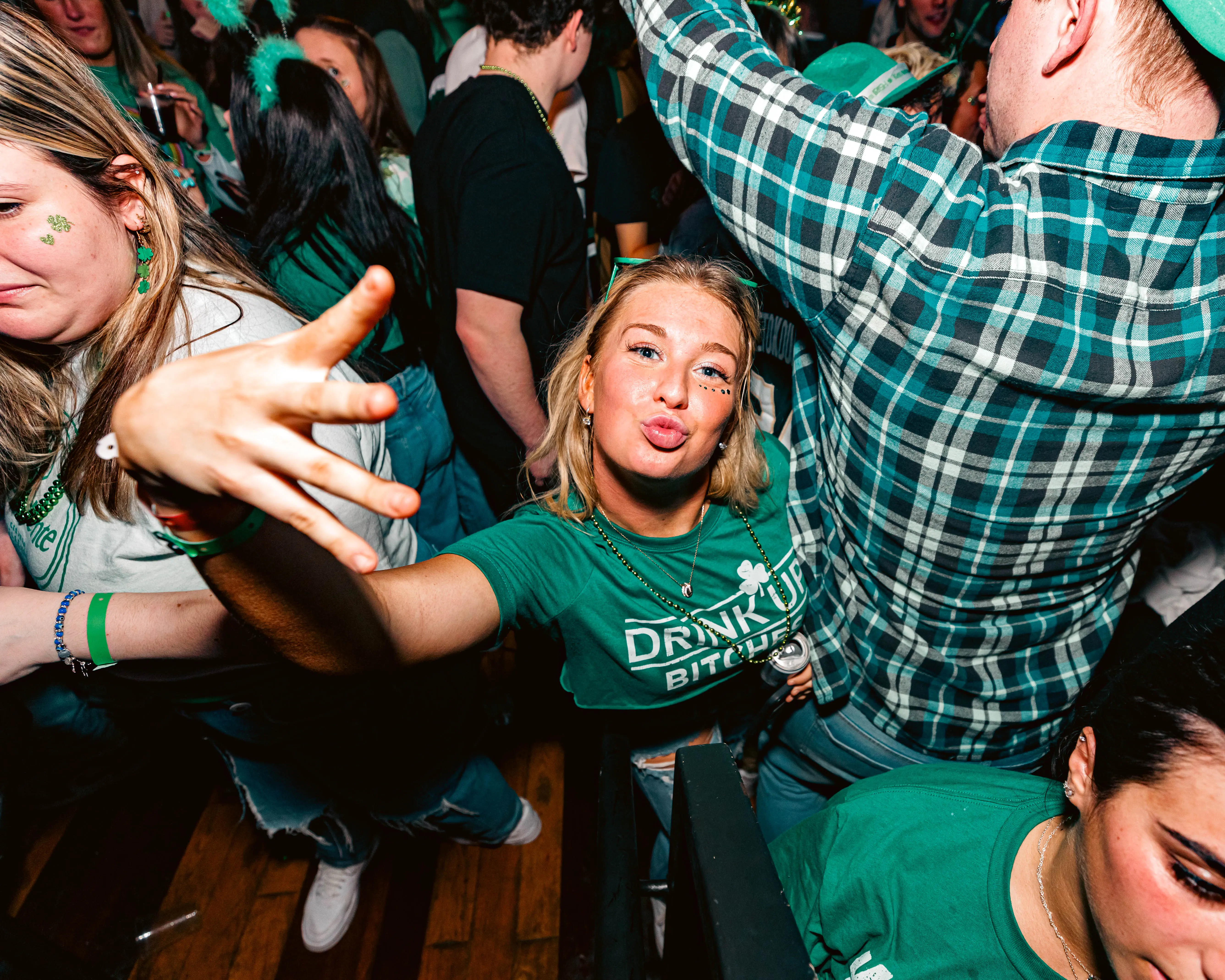 Woman in green reaching toward the camera in a packed bar celebration