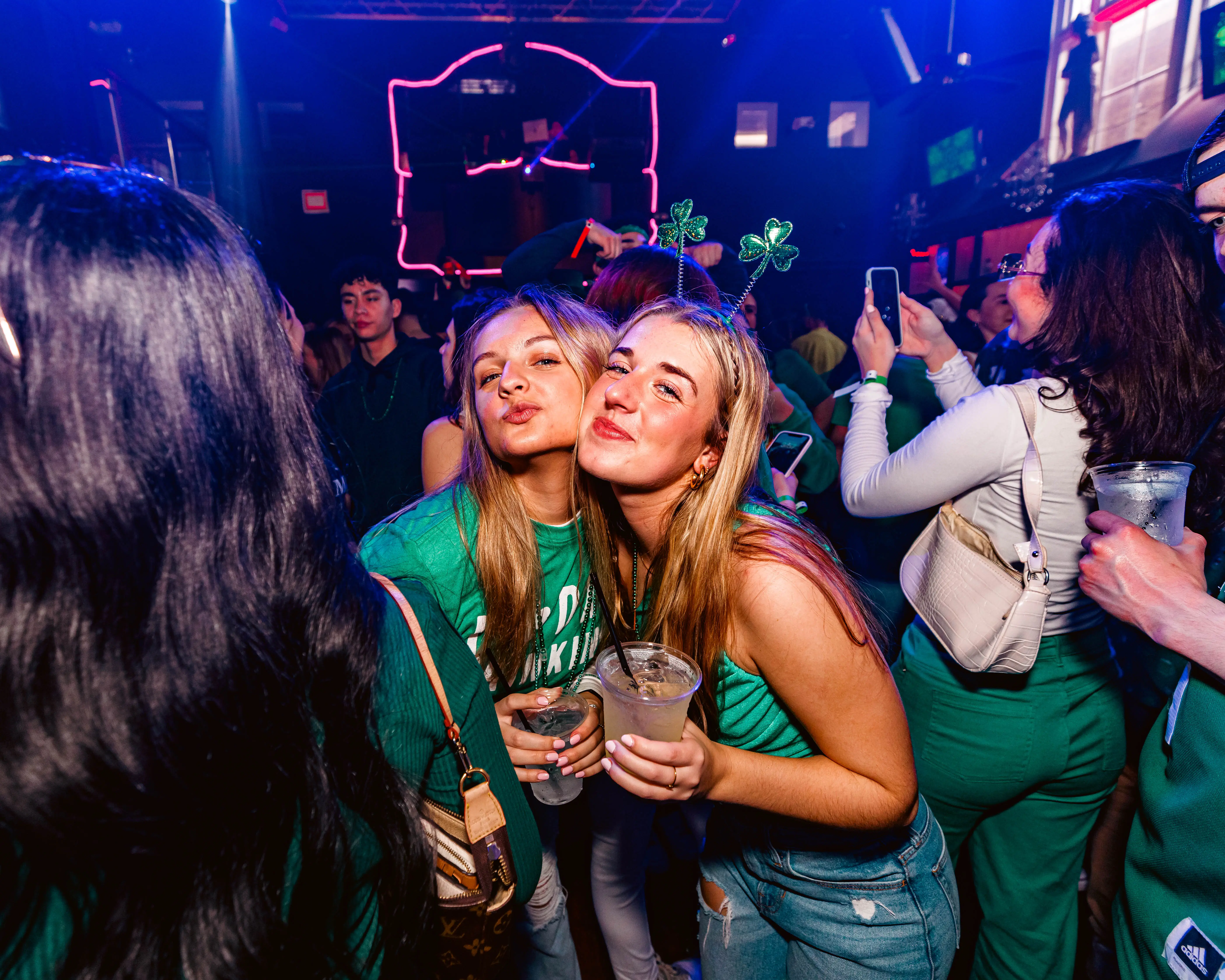 Two friends in green posing cheek to cheek under club lights