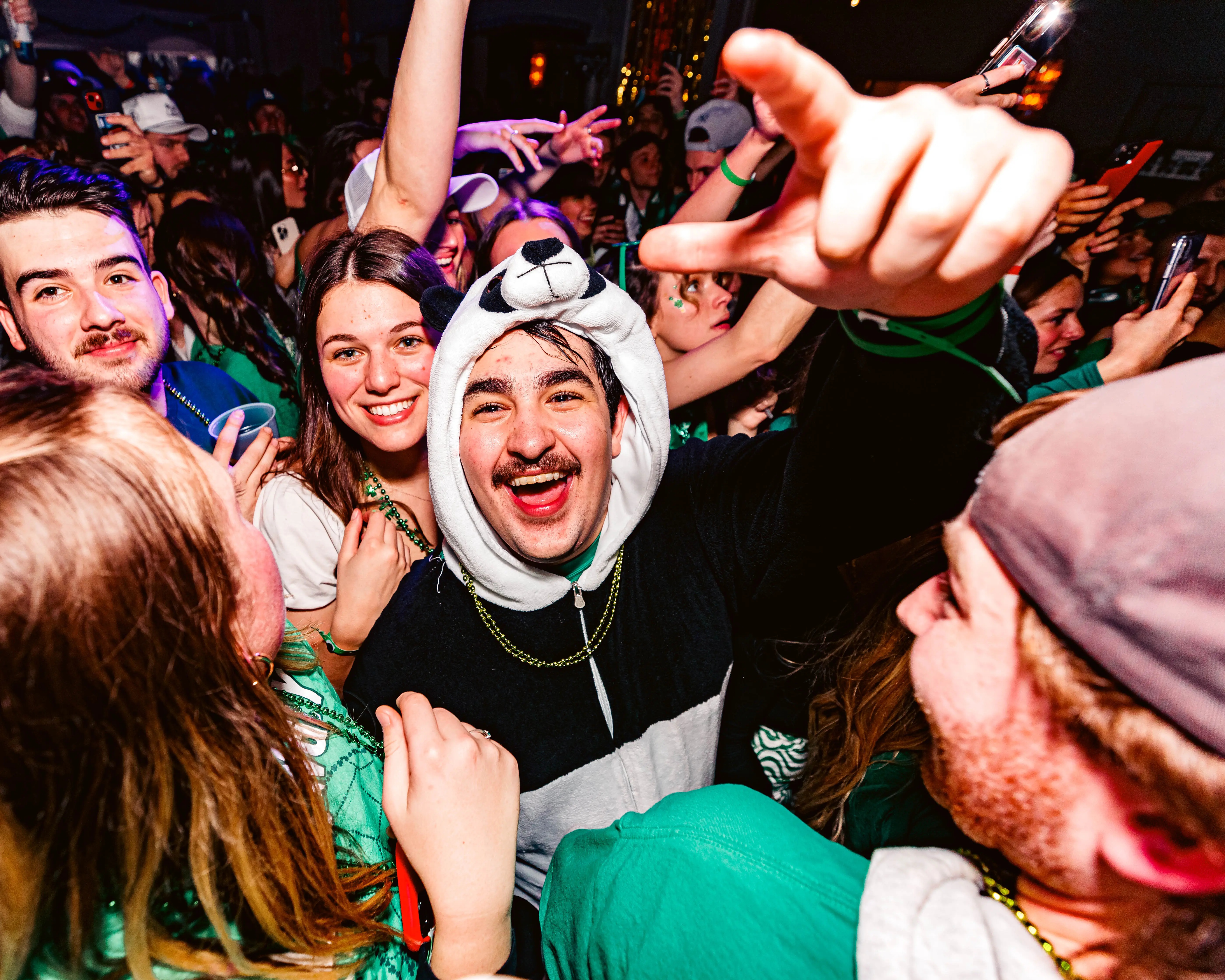 Grinning partygoer in a panda hood surrounded by a green-clad holiday crowd