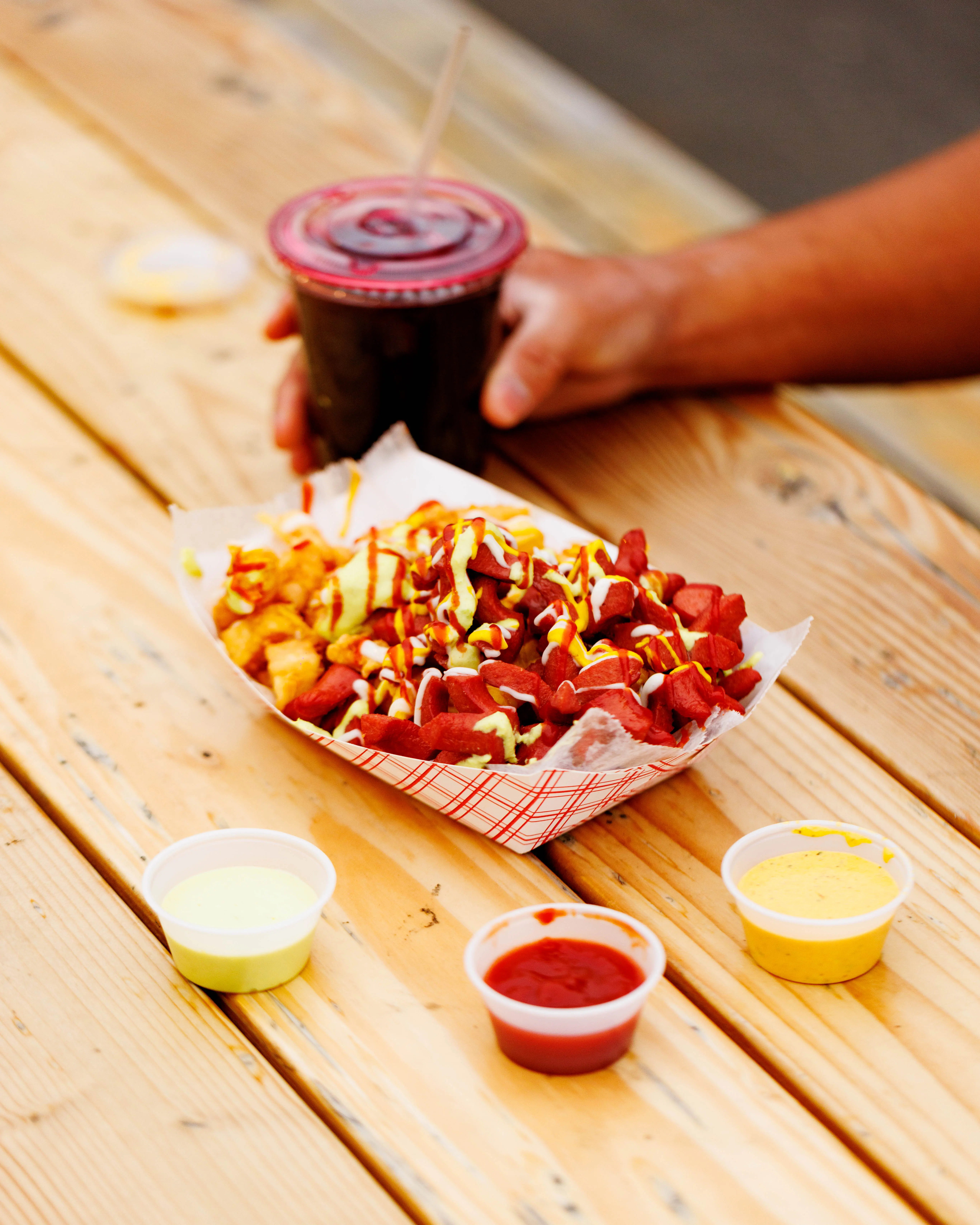 Loaded fries drizzled with sauces in a paper tray beside three dips