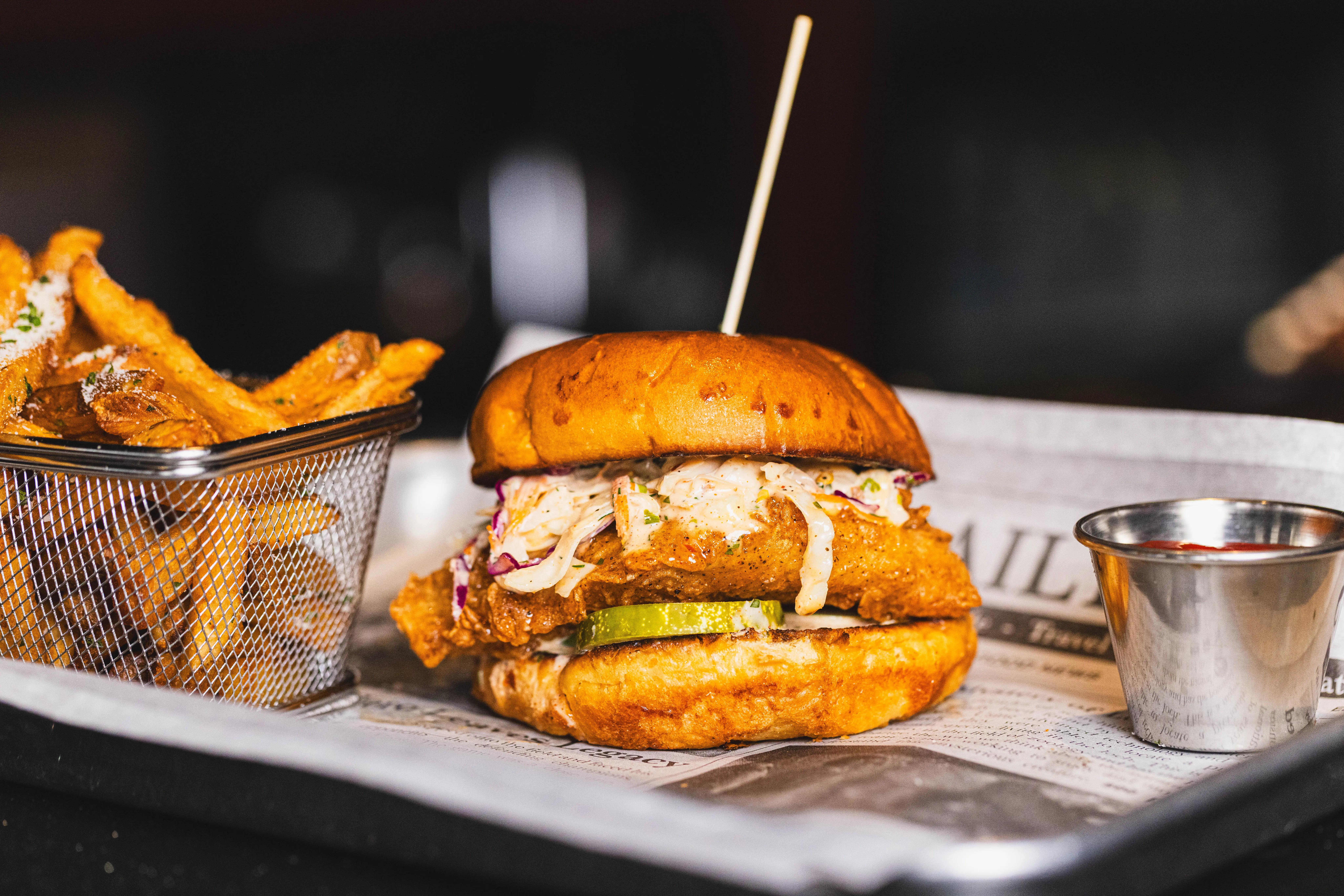 Fried chicken sandwich with pickles and slaw beside a basket of fries