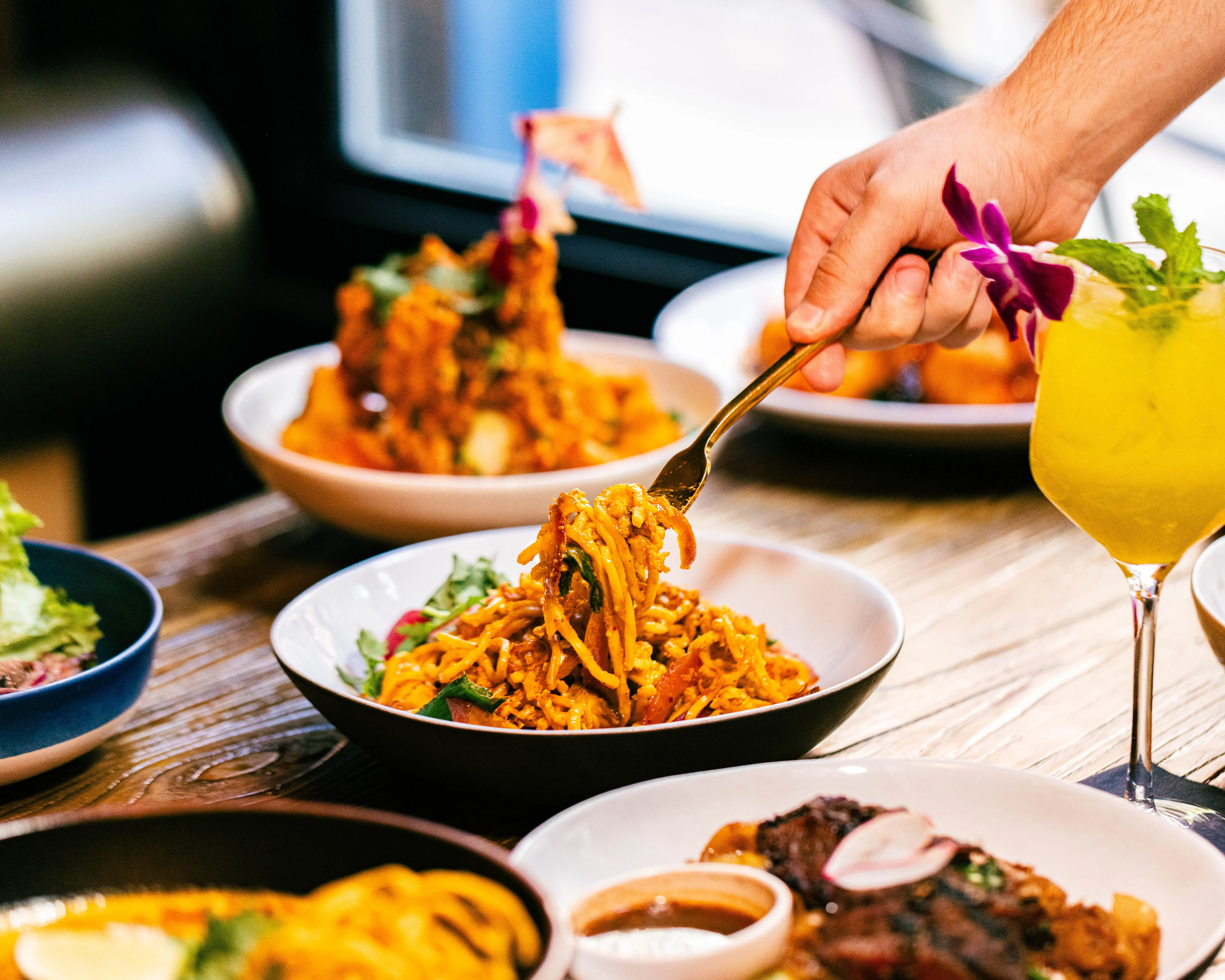 Fork lifting stir-fried noodles from a plated dish at a busy table