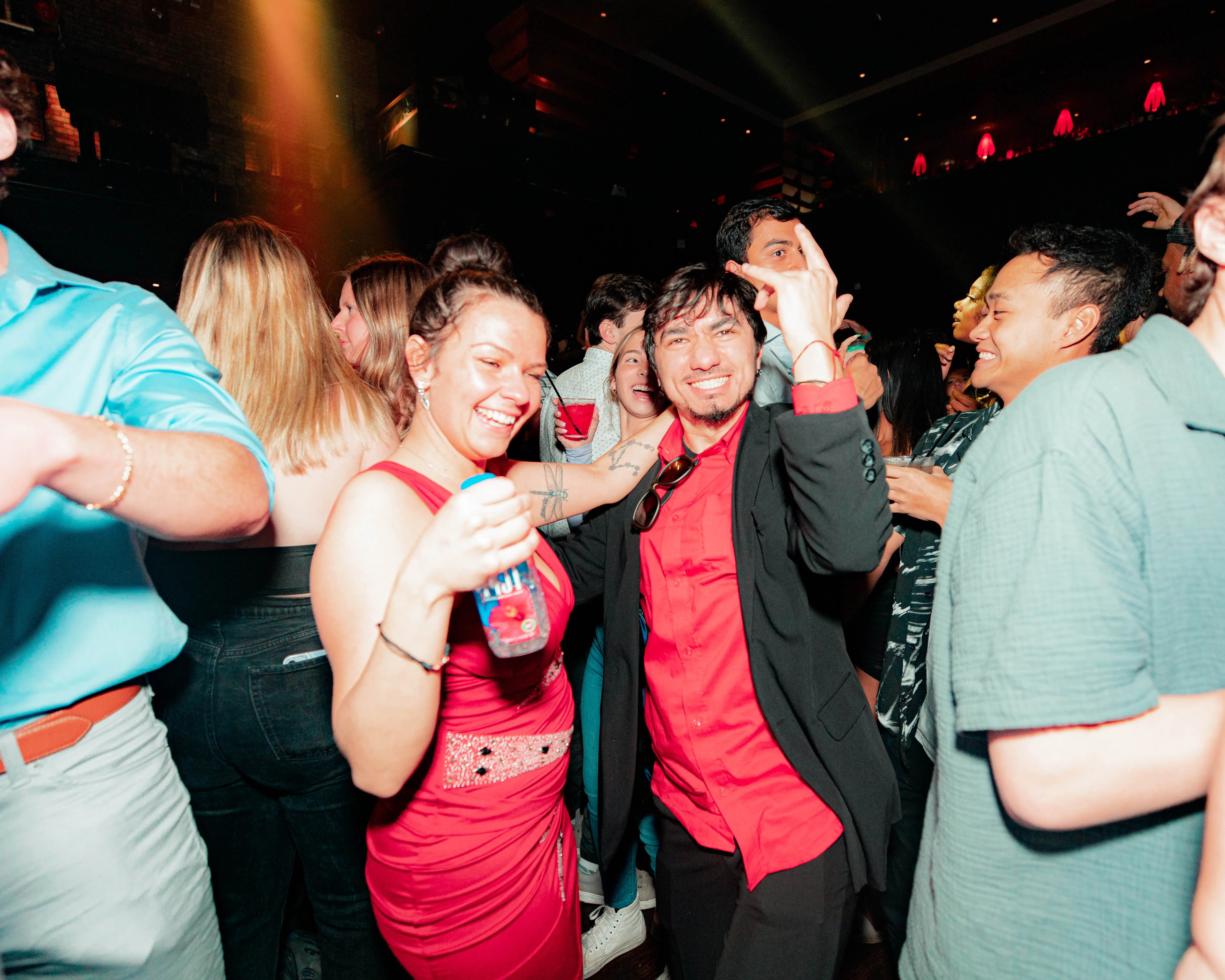 Two friends in red laughing together amid a crowded nightlife party