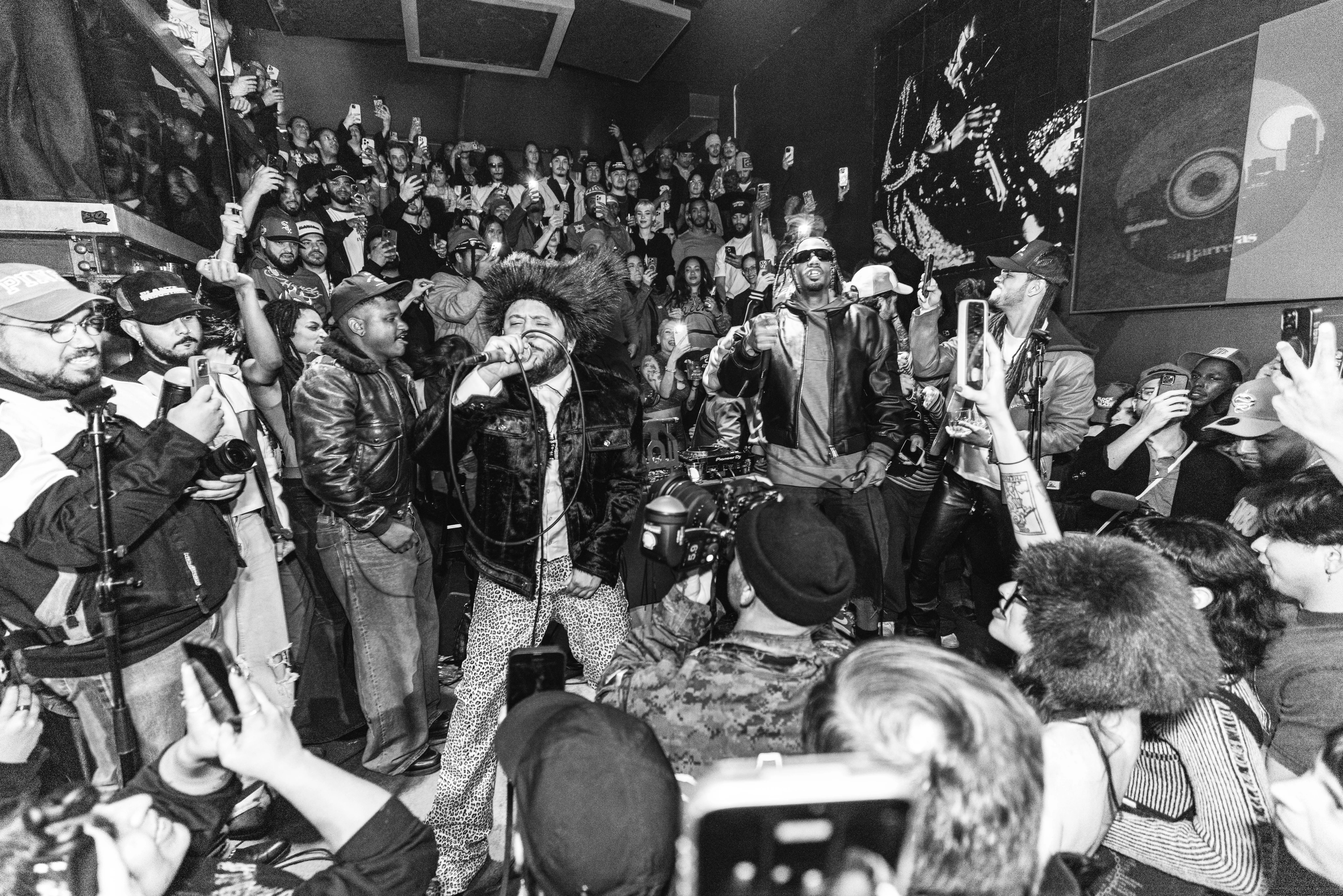 Black and white crowd raising phones as performers take a packed stage
